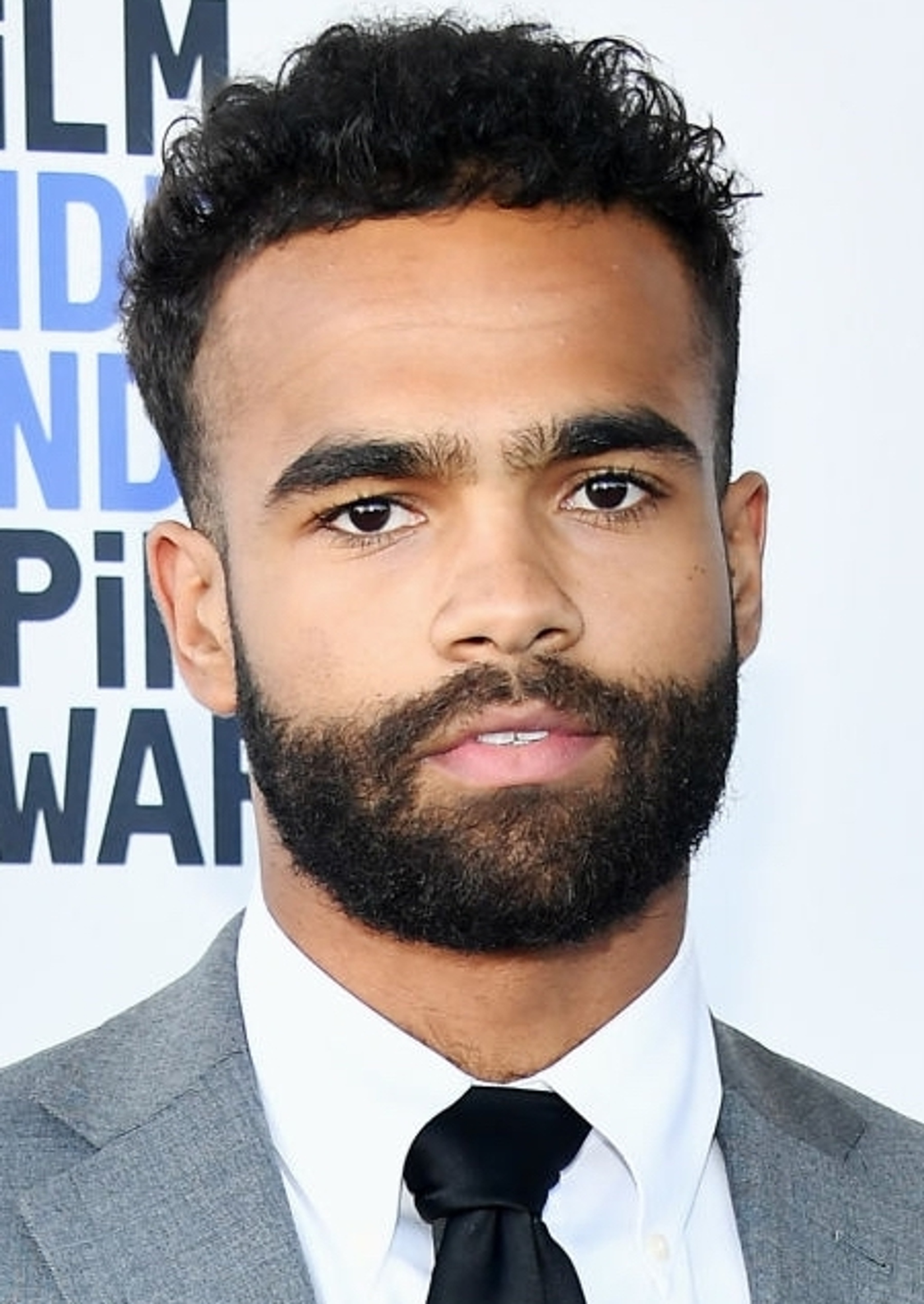 A headshot of director Phillip Youmans in a suit and tie with a dark beard