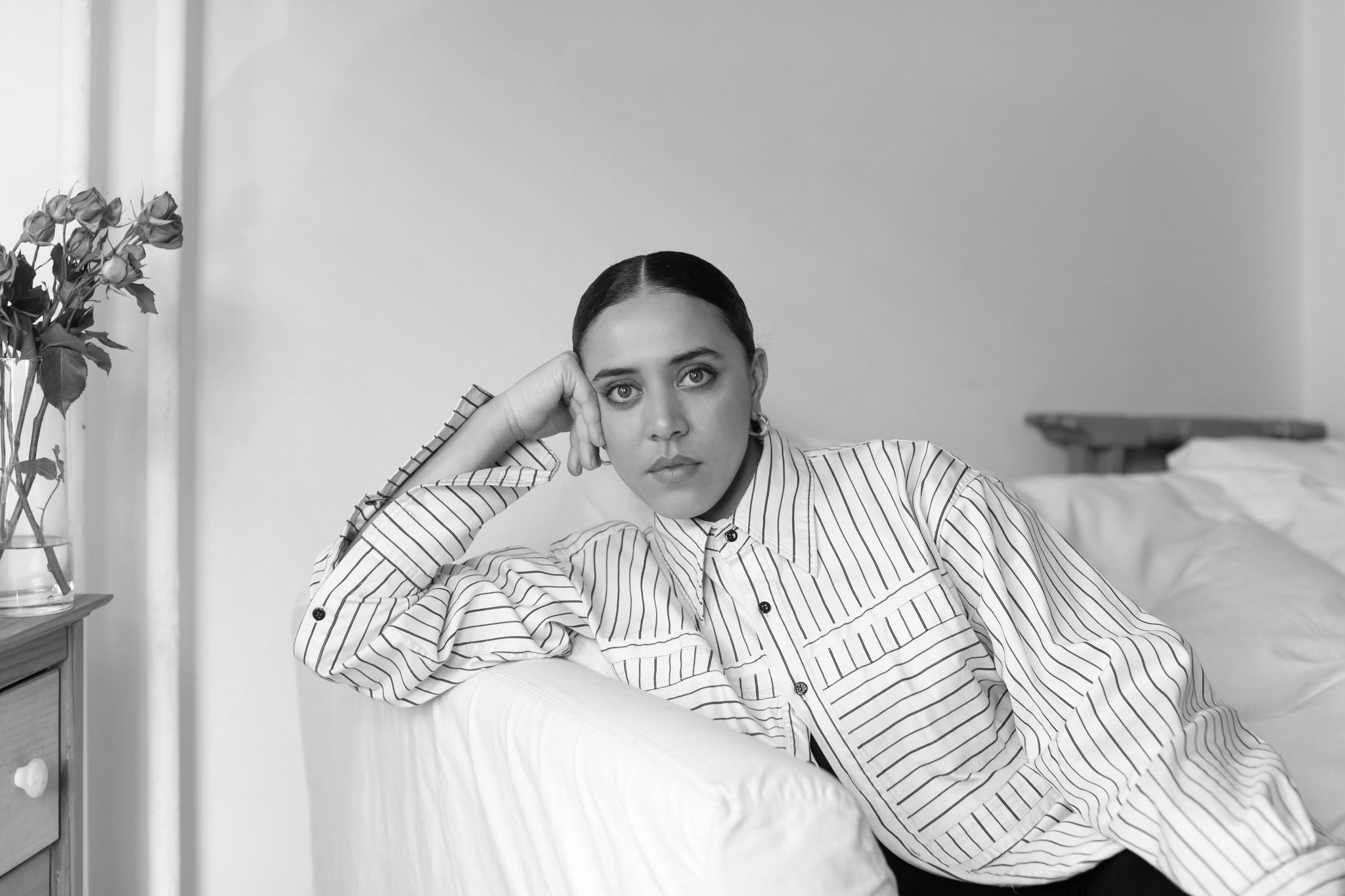 The artist Keenan MacWilliam supporting her head with her hand against the arm of a sofa. She wears a shirt with a pattern of parallel lines. 