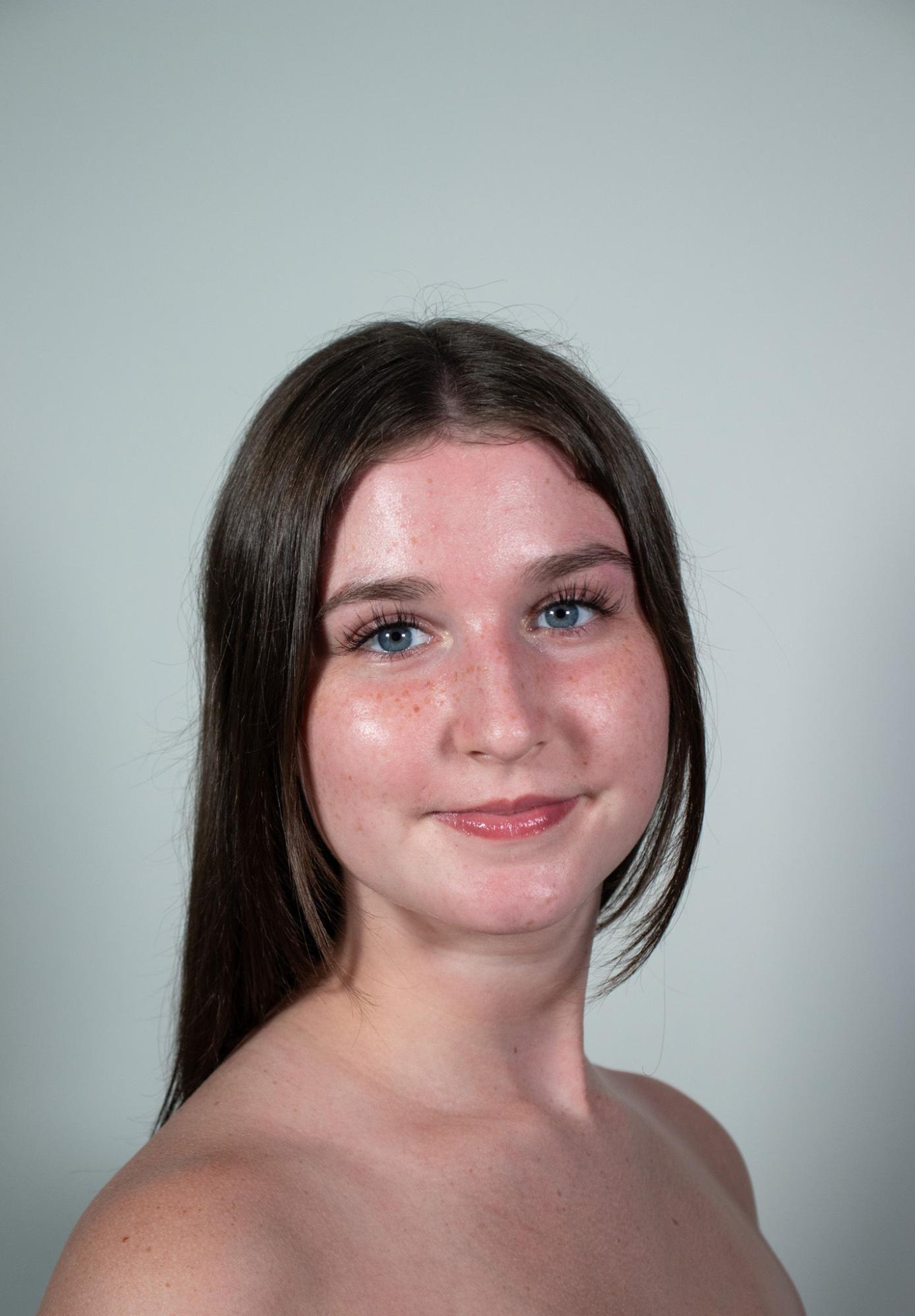 A headshot of dancer Sydney Jaffe, a white woman with straight brown hair pulled back to hang down behind her shoulders. She looks at us with a pleasant expression, smiling with her cheeks but mouth still closed. 