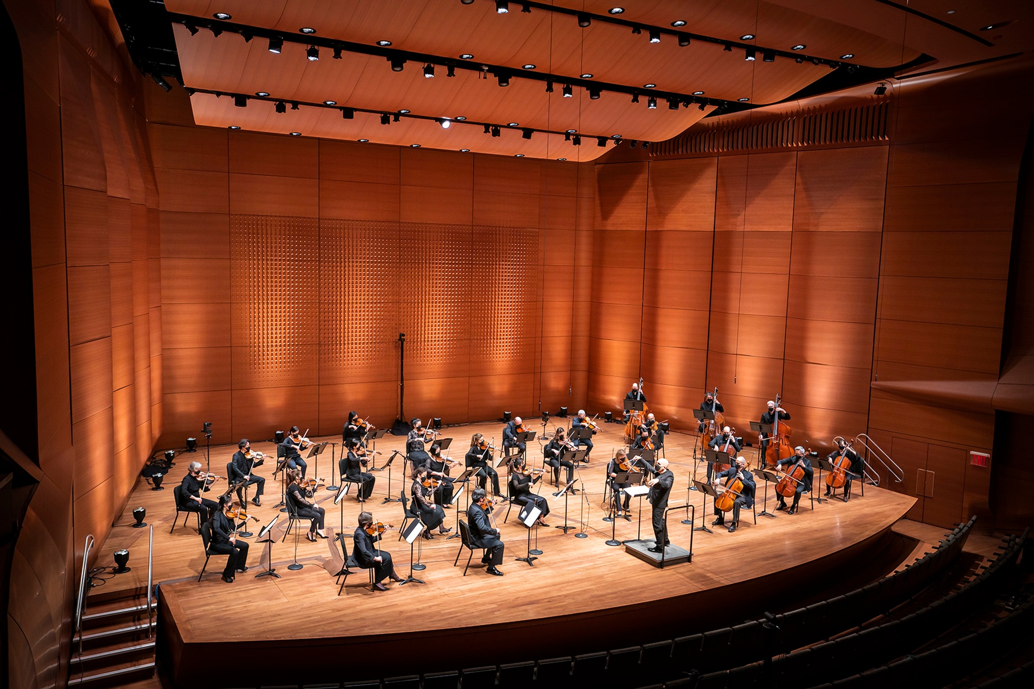 An orchestra sitting on a stage lit with warm lights against the background wall during a performance