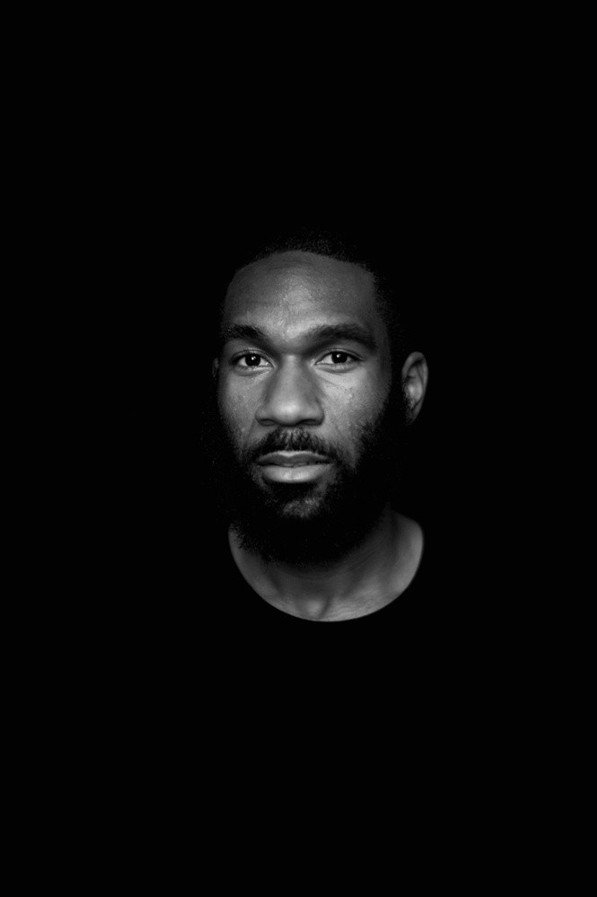 A portrait of Justin Allen wearing a black crewneck shirt against a black background