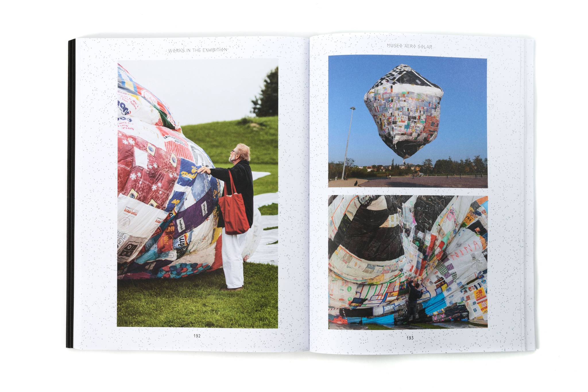 An exhibition catalogue lying open on a white surface. The book has white pages with large, full color images of artworks spread across them.