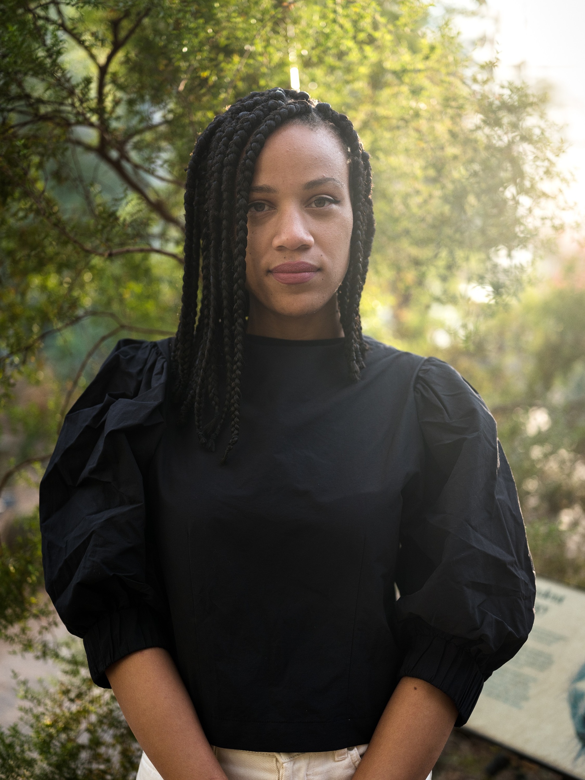 A portrait of curator Ashley James, with her hair parted slightly over one eye wearing a black blouse with puffy sleeves