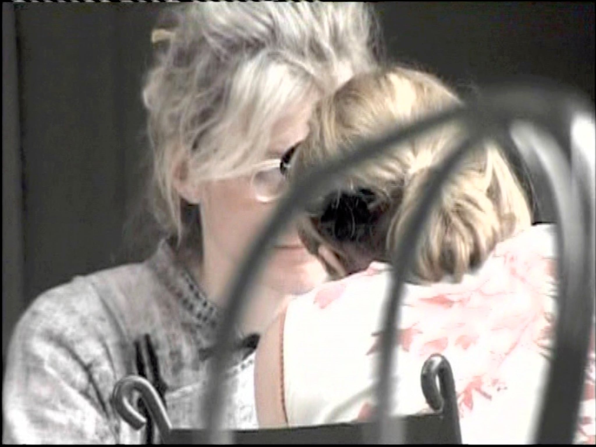 A woman with gray hair sits with her face obscured by the back of another woman's head. 