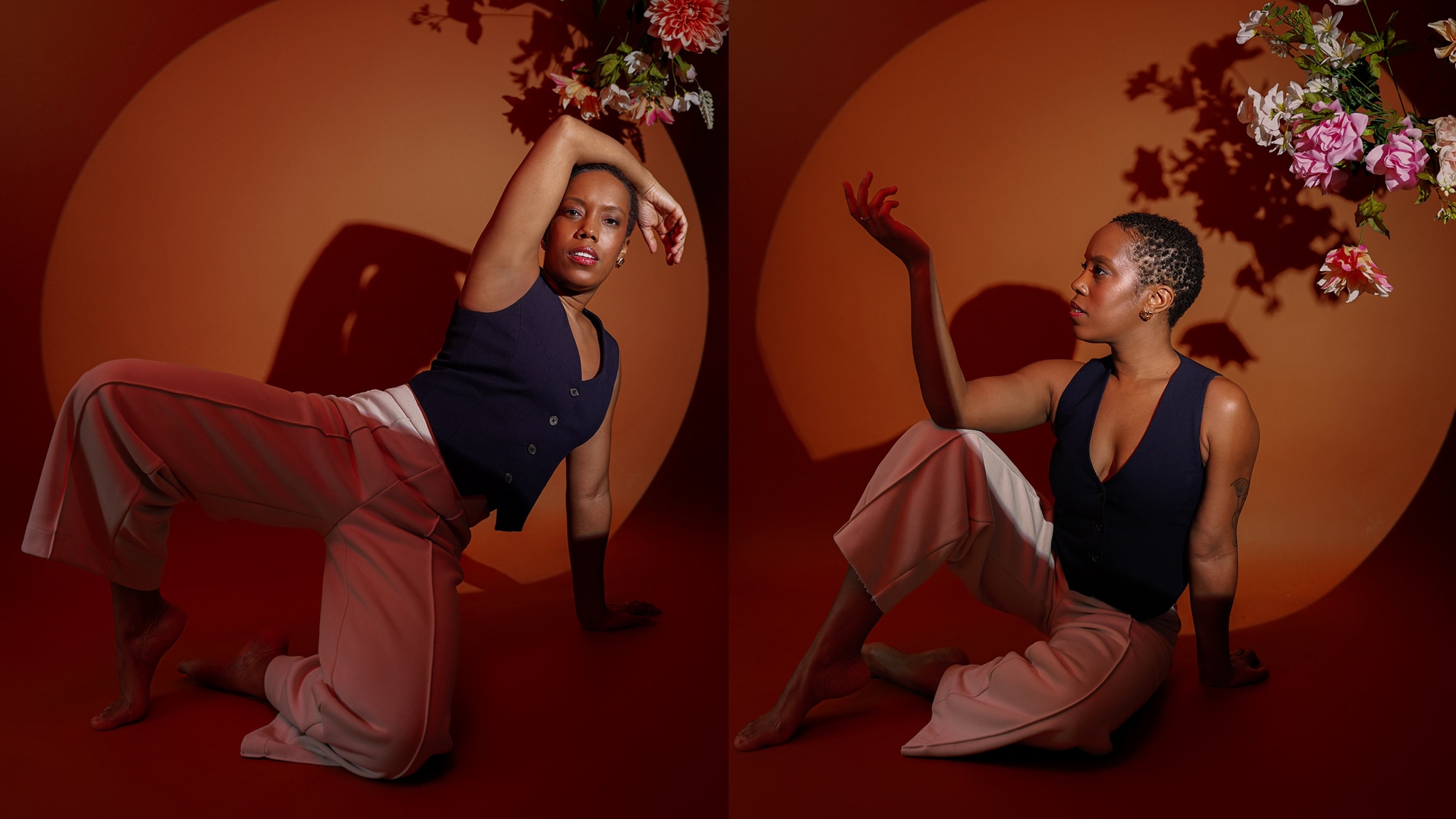 In two split screen portraits, Artist Tanya Birl-Torres, a Black woman with short hair, sits on the ground beneath a hanging bouquet of pink and white flowers against a burnt orange backdrop. In the right-hand image, she is seen in profile with one leg raised and one arm reaching up, propped on her knee. She wears a blue sleeveless top with a plunging v-neck and cream colored pants. In the left-hand image, she arches backward with one arm extended over her head.