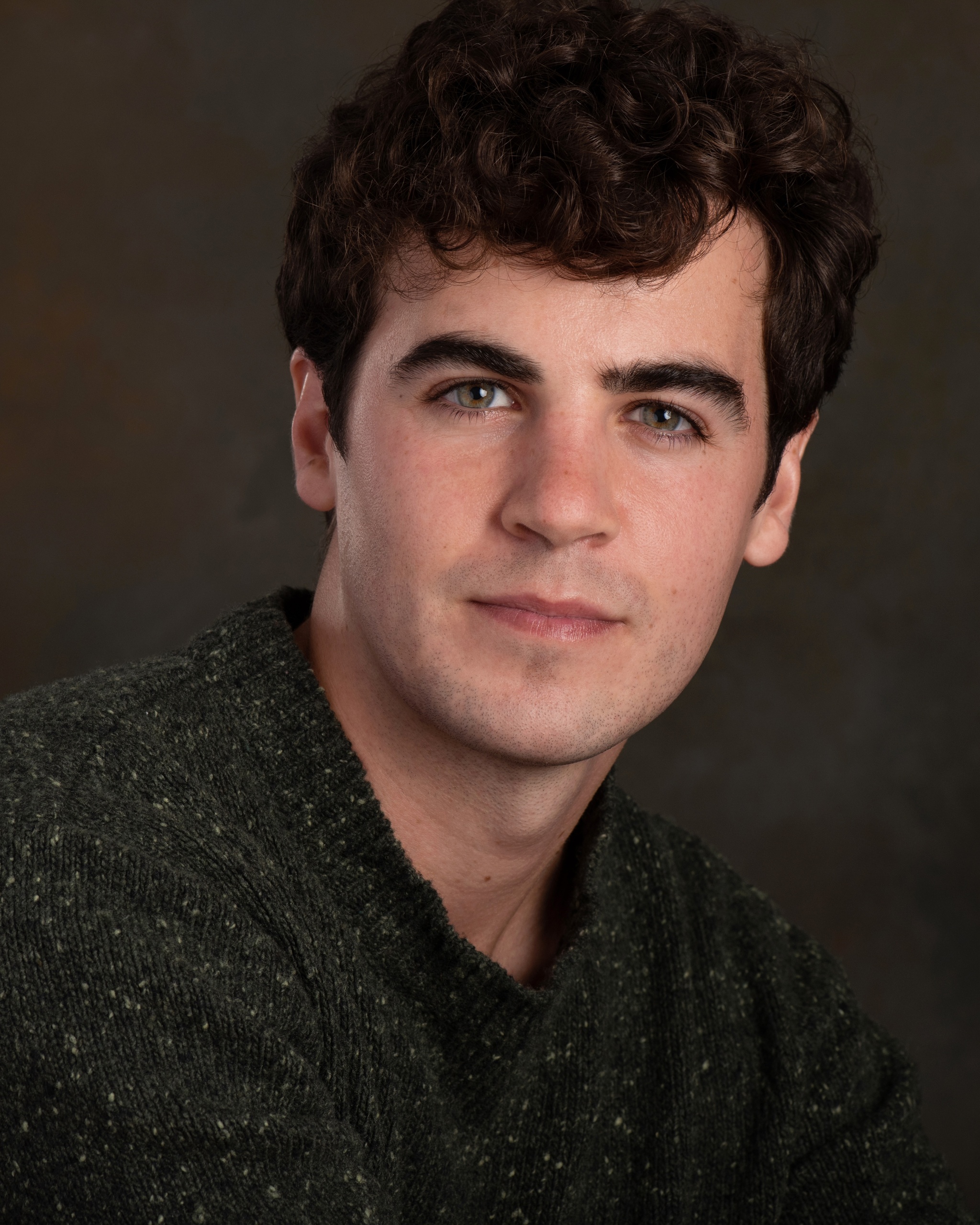 A headshot of actor Ian Bouillion, a white man with short dark brown hair and a swoop of bangs over his forehead. He looks directly at us inquisitively, with one eyebrow slightly raised.