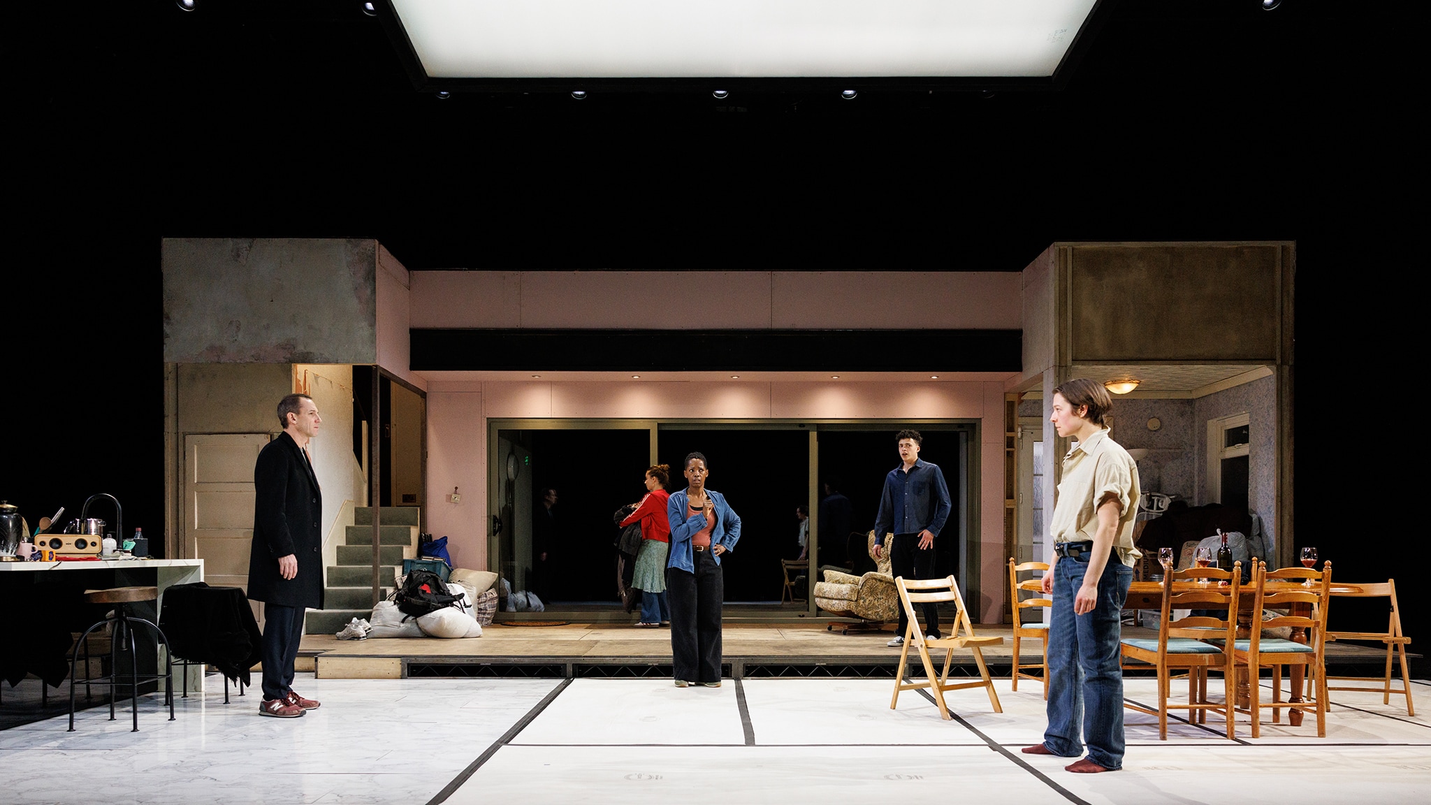 The cast of The Other Place is dispersed across the stage, on a set designed to look like a kitchen in a family home in the process of renovation, with a long sliding door window along the back wall. 