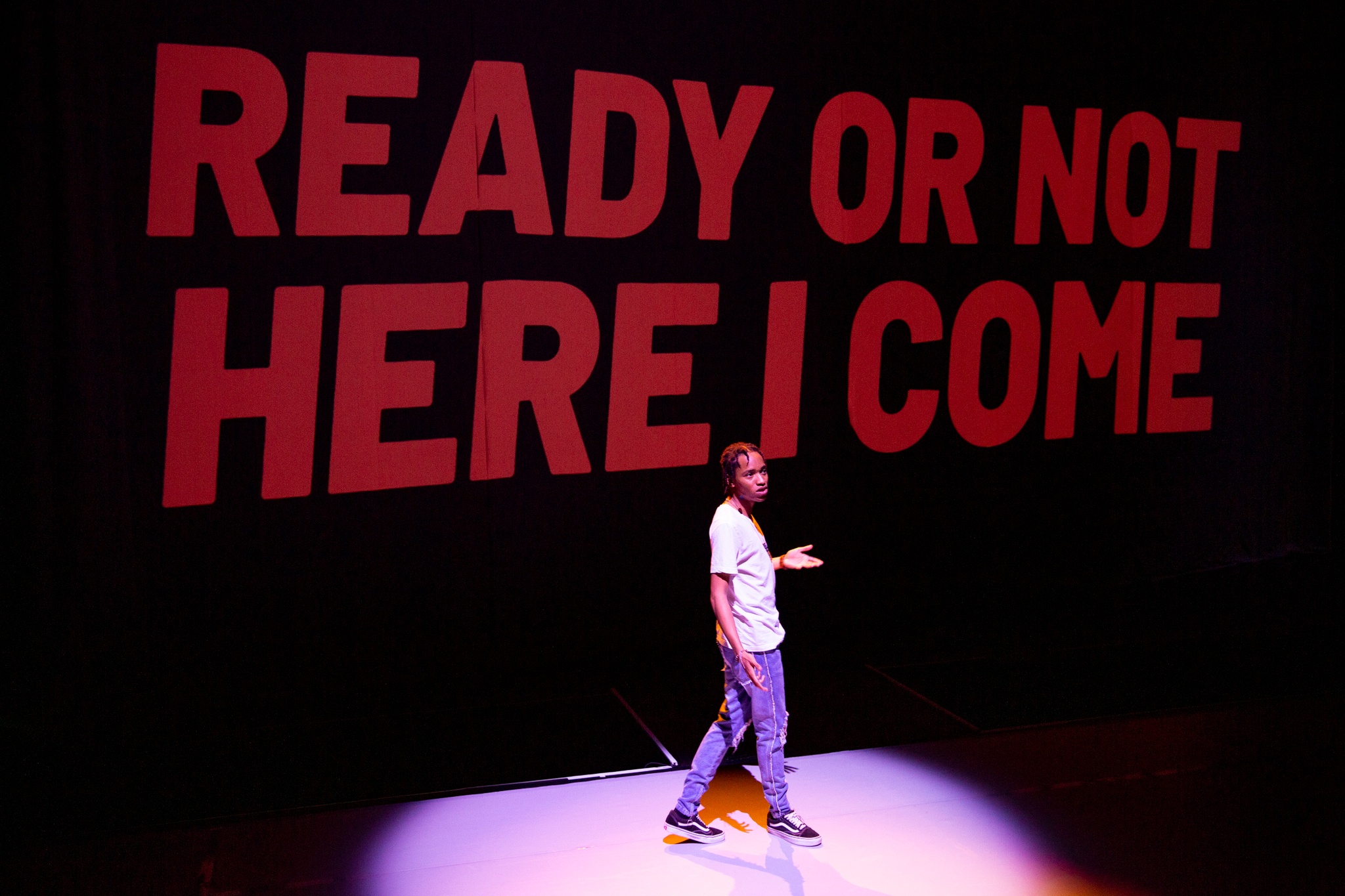 A POWERPLAY performer on stage in front of a background that reads Ready or not here I come