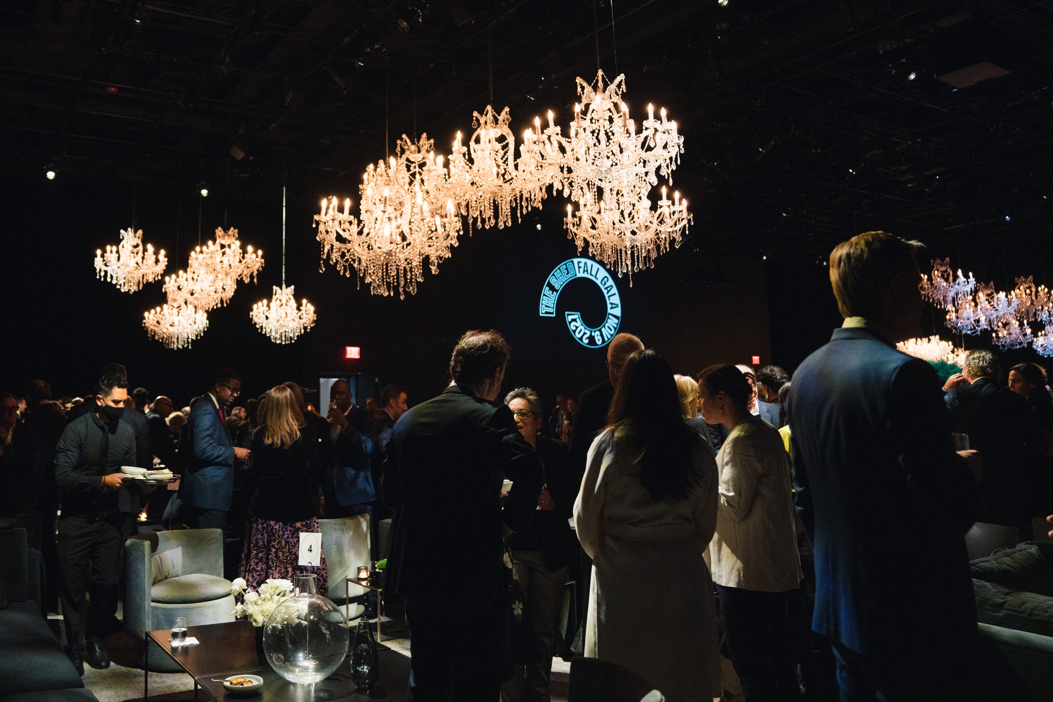 Gala guests mingle in a space lit by numerous chandeliers that shimmer above their heads.