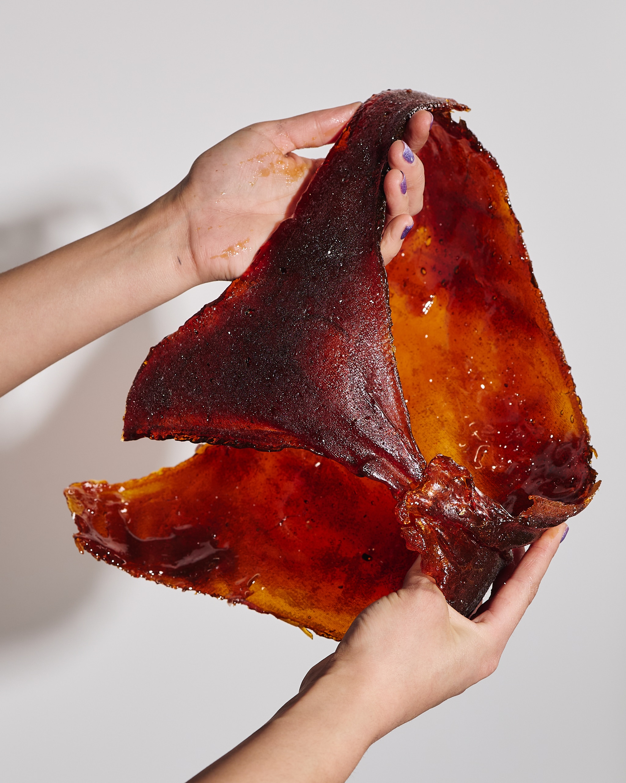 The hands of artist Mel Corchado are seen as she holds a cast-sugar garment. The garment resembles a pair of women's underwear or bathing suit bottom and is a rich orange-brown color.