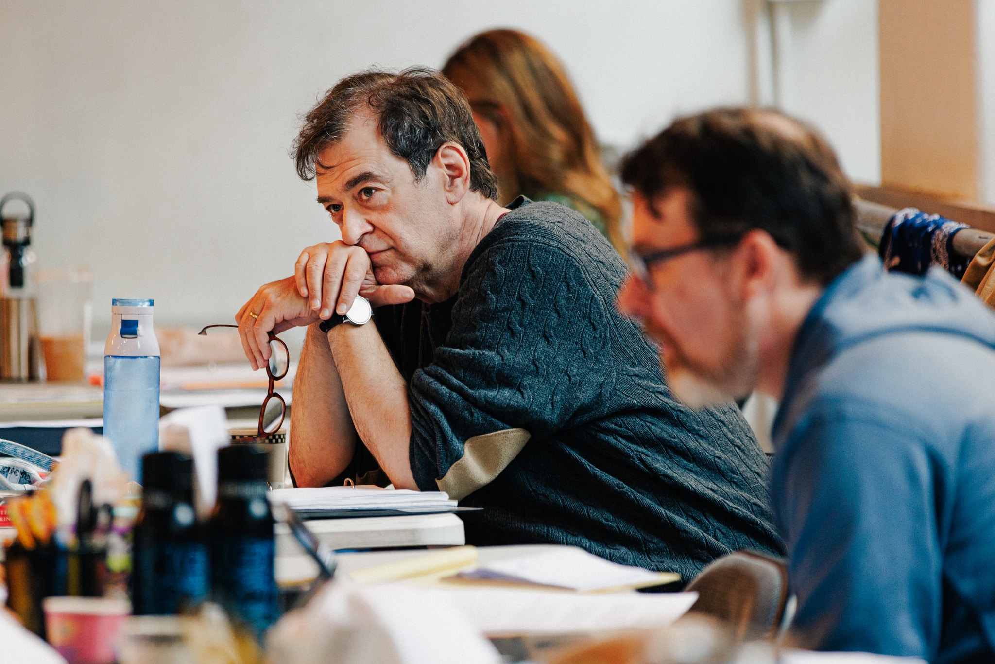 A photo of writer James Glossman leaning over a desk with hands clasped to his face while he leans on his elbows. He is absorbed by something out of frame and we see him in profile.