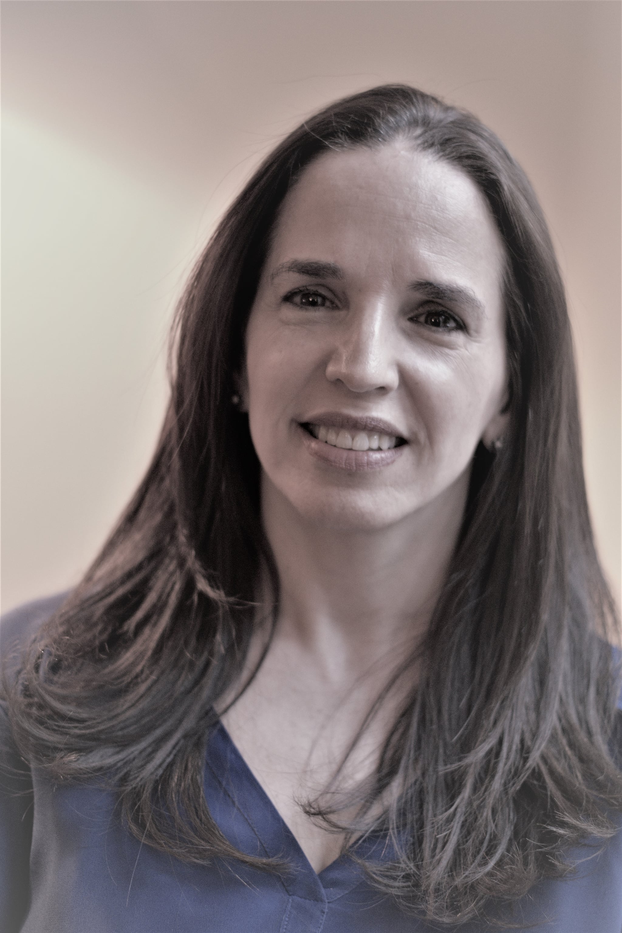 A woman with hair falling beneath her shoulders smiles. She wears a pale-purple v-neck sweater. 