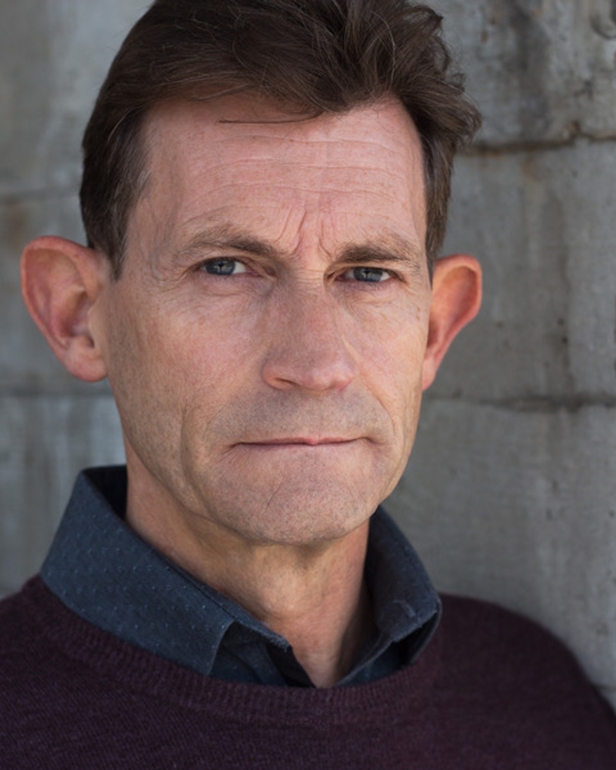 A portrait of actor David Bromley, a white man with short brown hair combed to the side. He has an interested, intent look on his face.