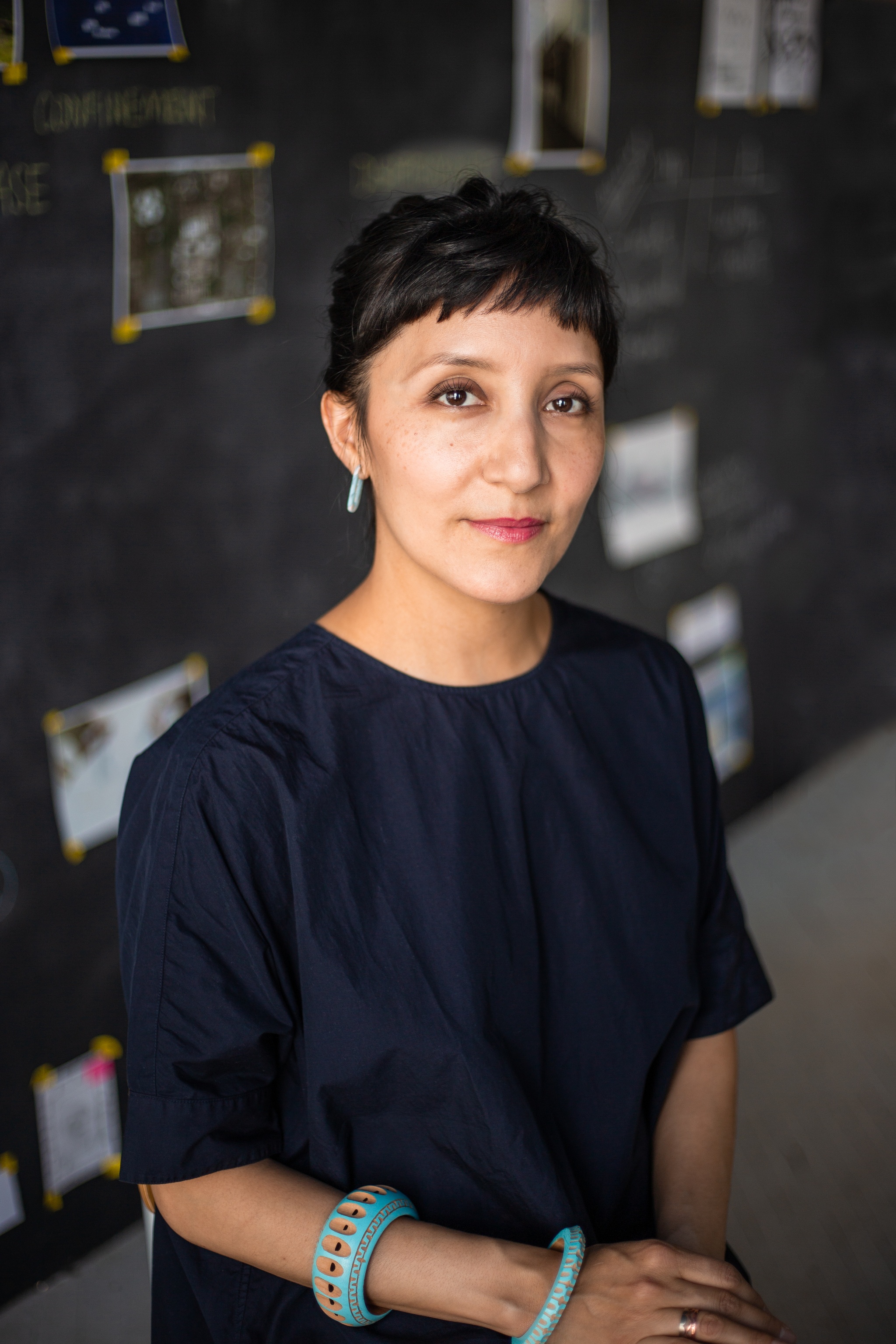 A photo of Maria Gaspar wearing a dark blue dress and two turquoise bracelets. She has short bangs with her hair pulled back. 