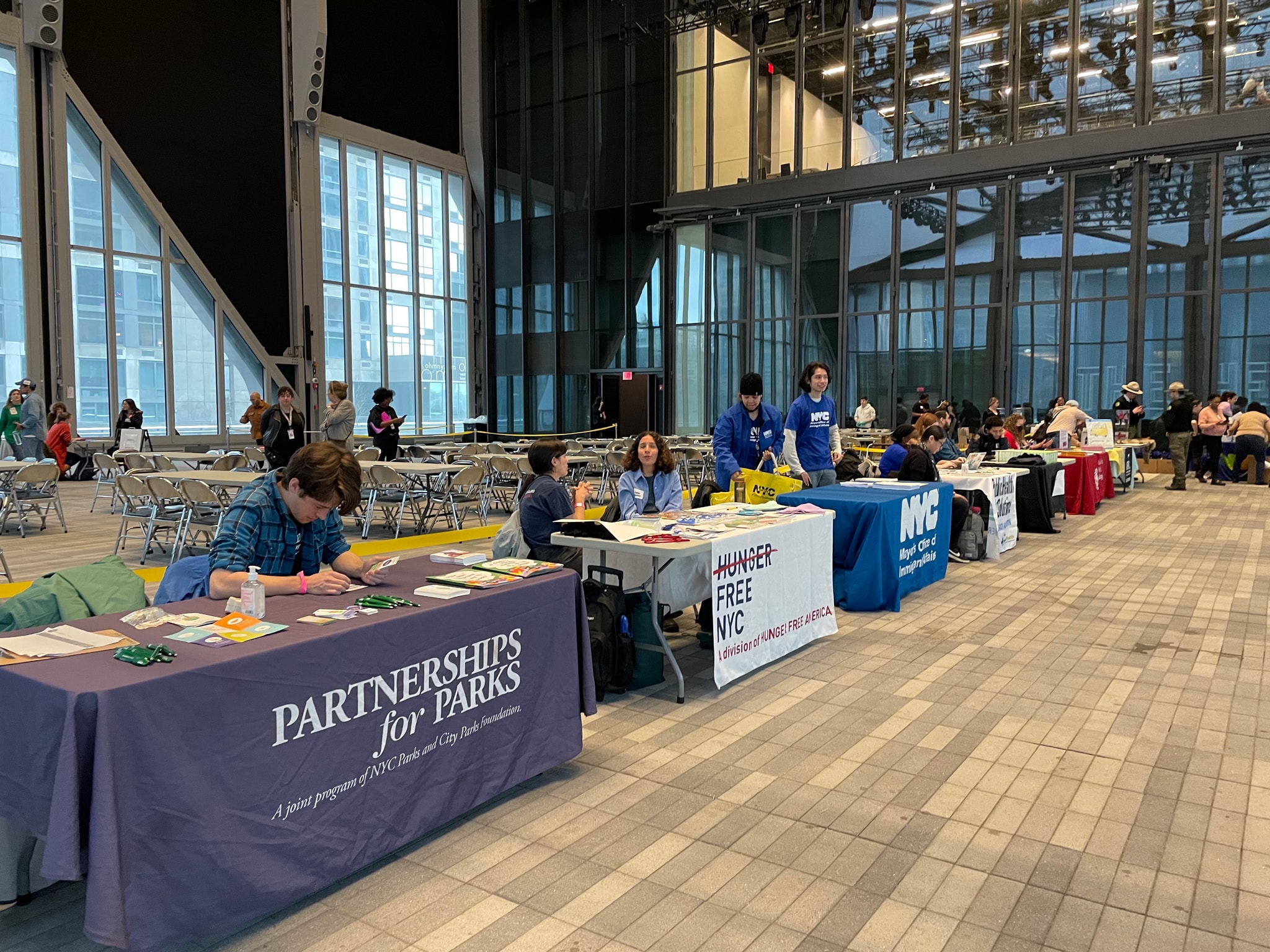 A line of tables set up with organizations providing services at a resource fair. Each table is covered by a tablecloth with the organization's name.