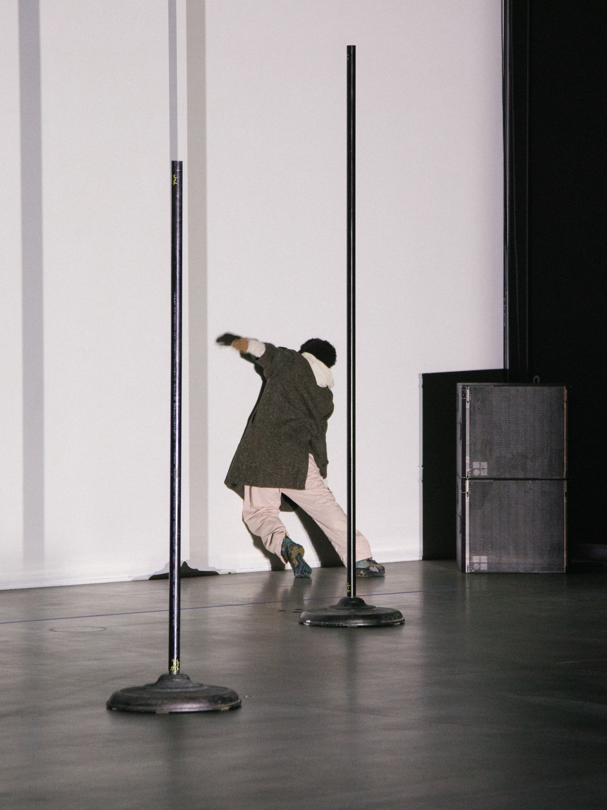 The artist Niall Jones leans the weight of his body against a white wall during a performance so that he is supported by the force of his body. He is facing the wall so his face is not visible.