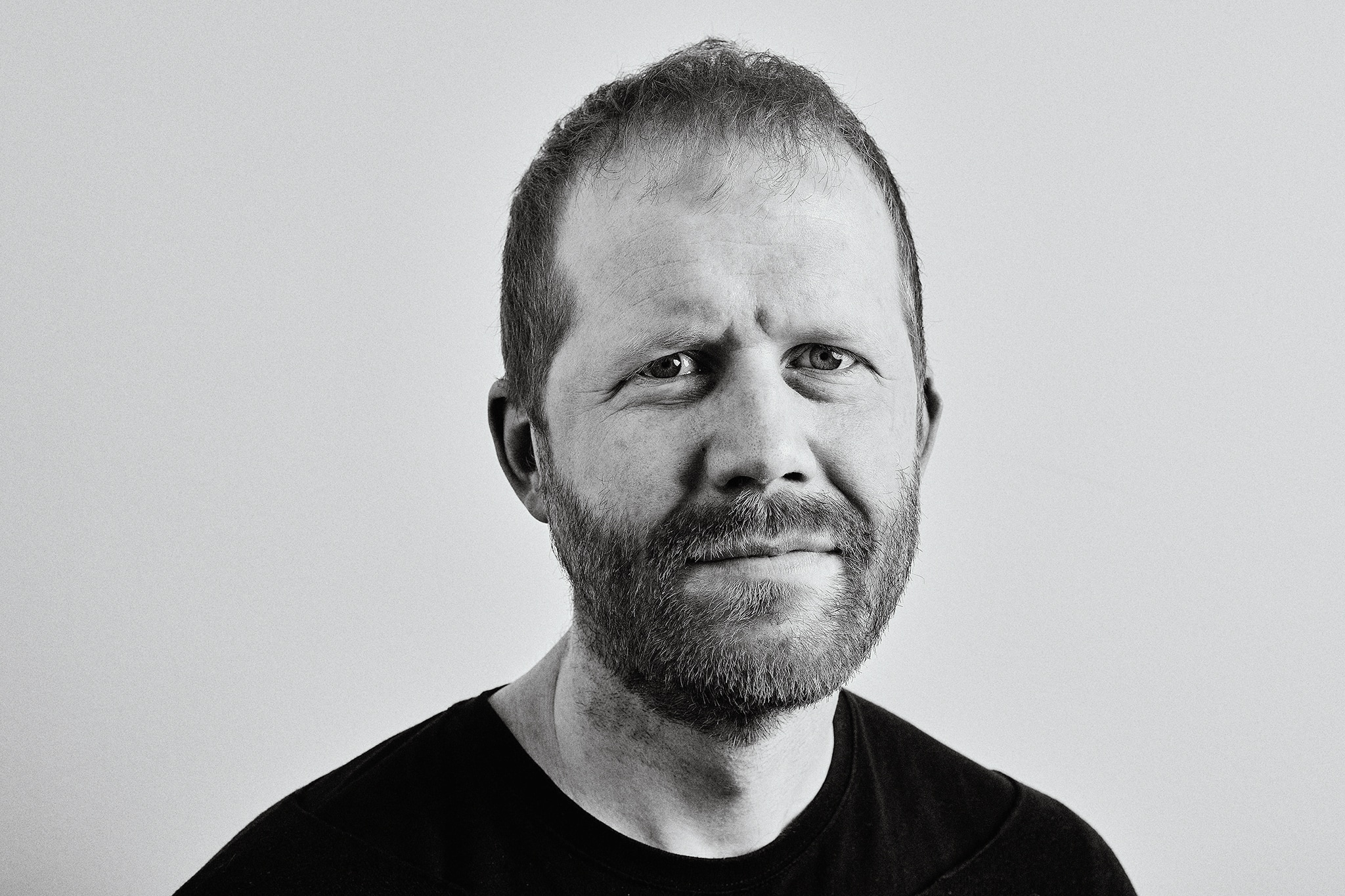 A white man with a beard wearing a black crewneck shirt furrows his brow.
