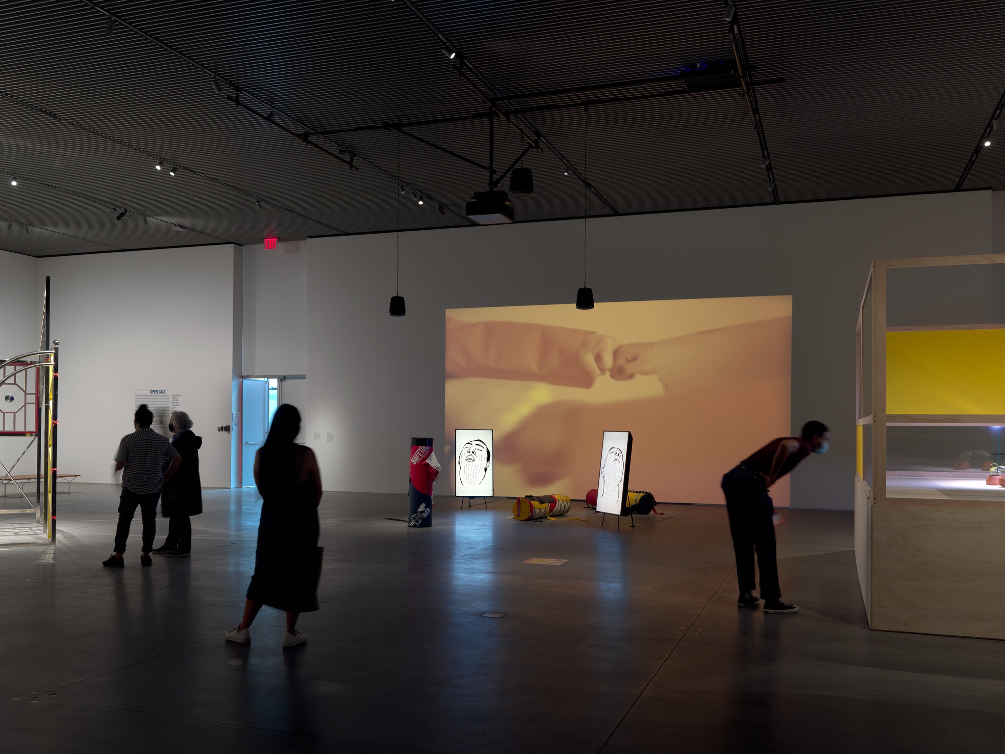 An art installation including a film projected on a gallery wall, two vertical video screens sitting on the floor accompanied by two stuffed tackling dummies.