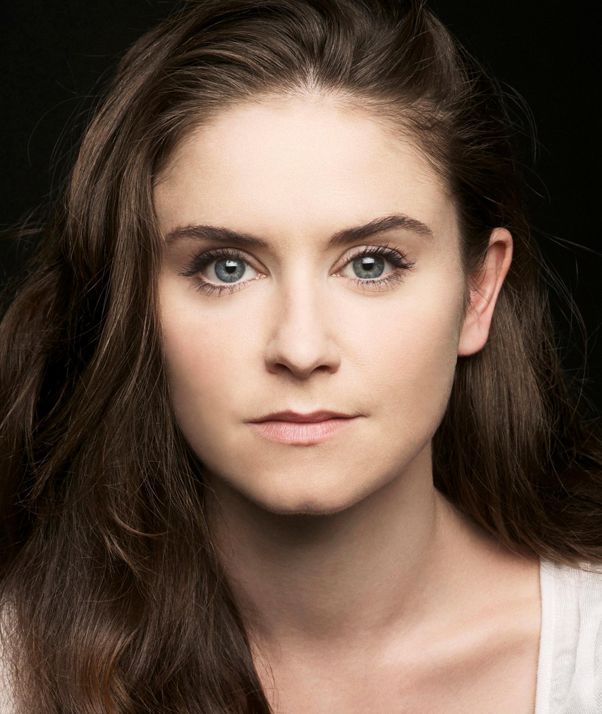 A headshot portrait of actor Judith Roddy, a white woman with long brown hair flowing beneath her shoulders. She looks directly at the camera and smiles slightly without opening her mouth.