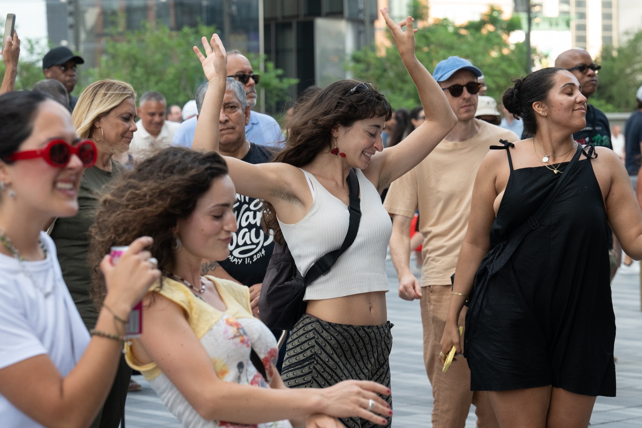 A group of people in tank tops and t-shirts dance wildly with arms outstretched and smiles on their faces on a hot summer afternoon. 