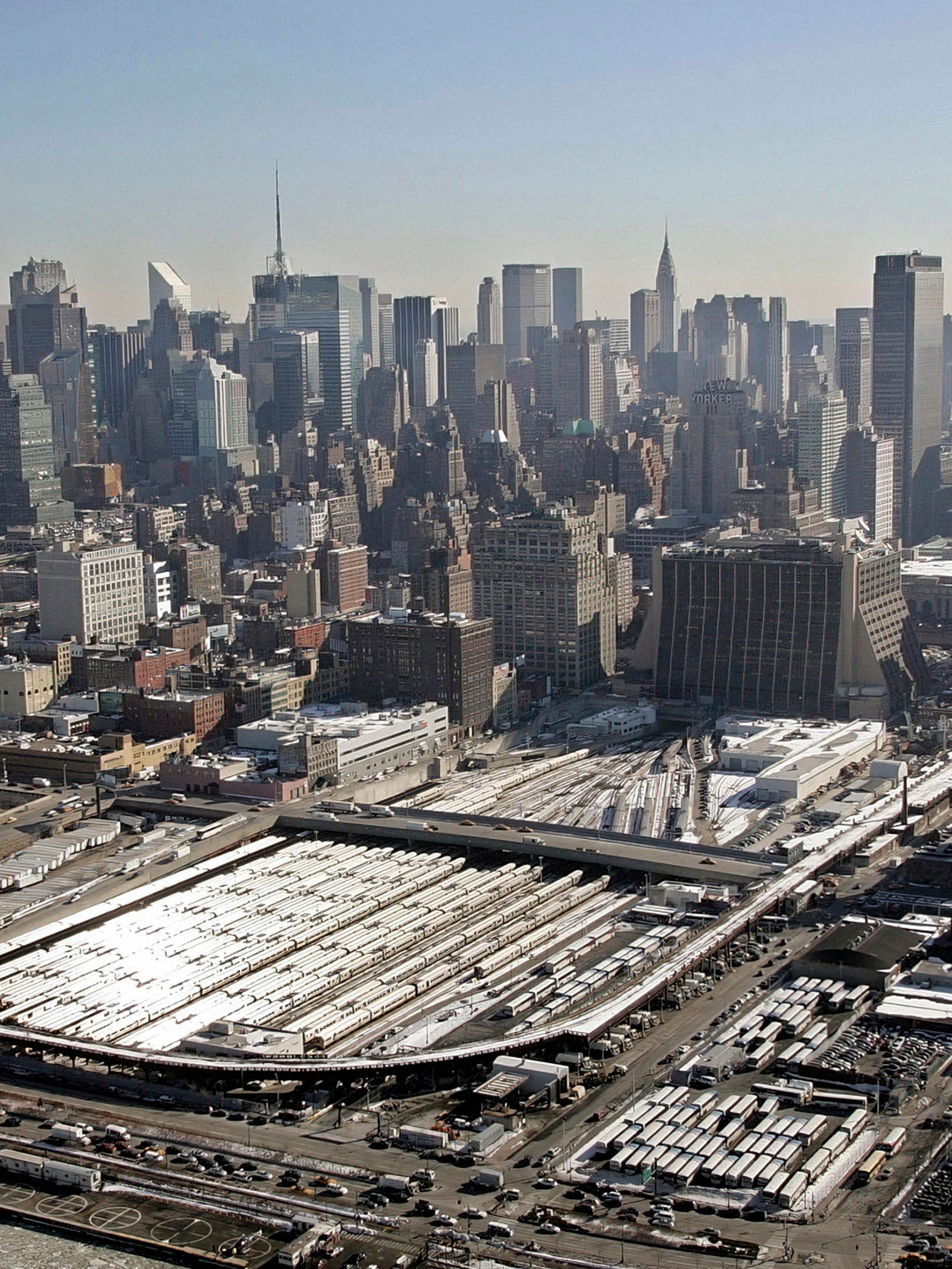 The New York skyline seen on a sunny day from the west side above the Hudson River. Prominent in the foreground are the rail yards covering multiple blocks before the development of Hudson Yards.