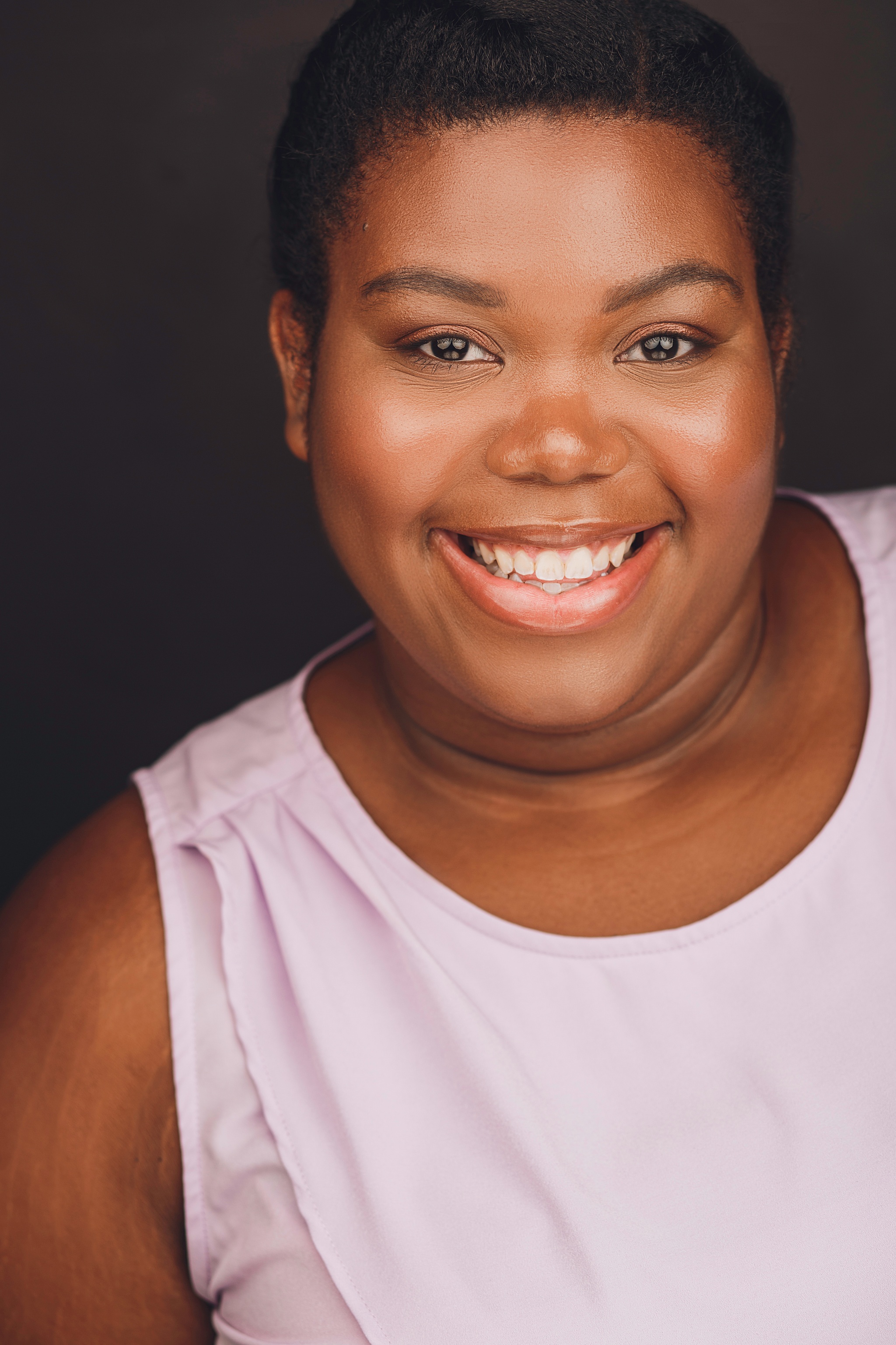 A Black woman with short hair pulled back behind her head. She is wearing a pink tank top and smiling.