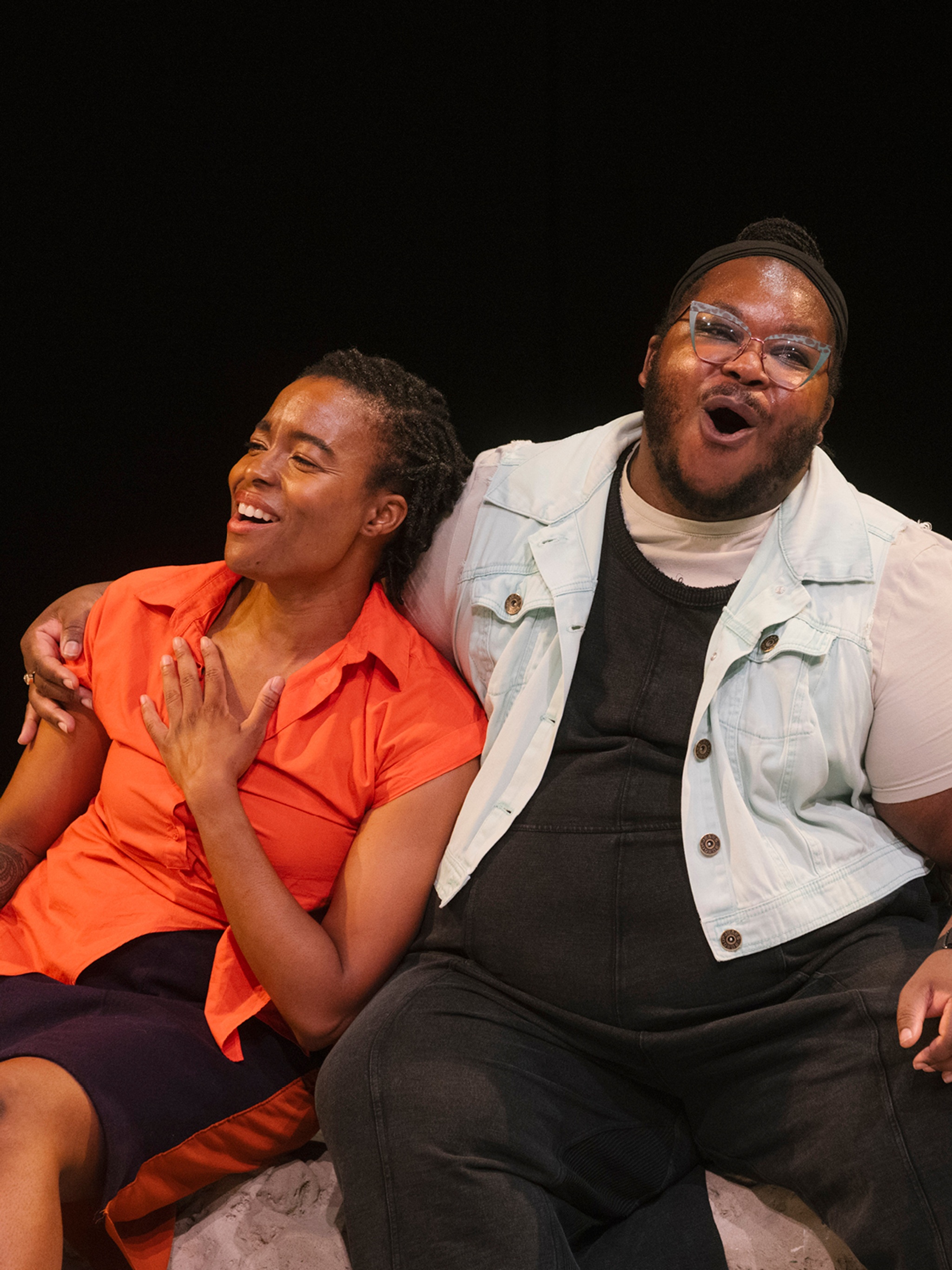 Nicole Y. McClam, a Black woman, leans on Azure D. Osborne-Lee, a disabled Black trans and queer person, as they sit and sing out joyfully. Azure has their arm around Nicole’s shoulders, as Nicole rests a hand on her chest. Photo by Ahad Subzwari/The Shed.