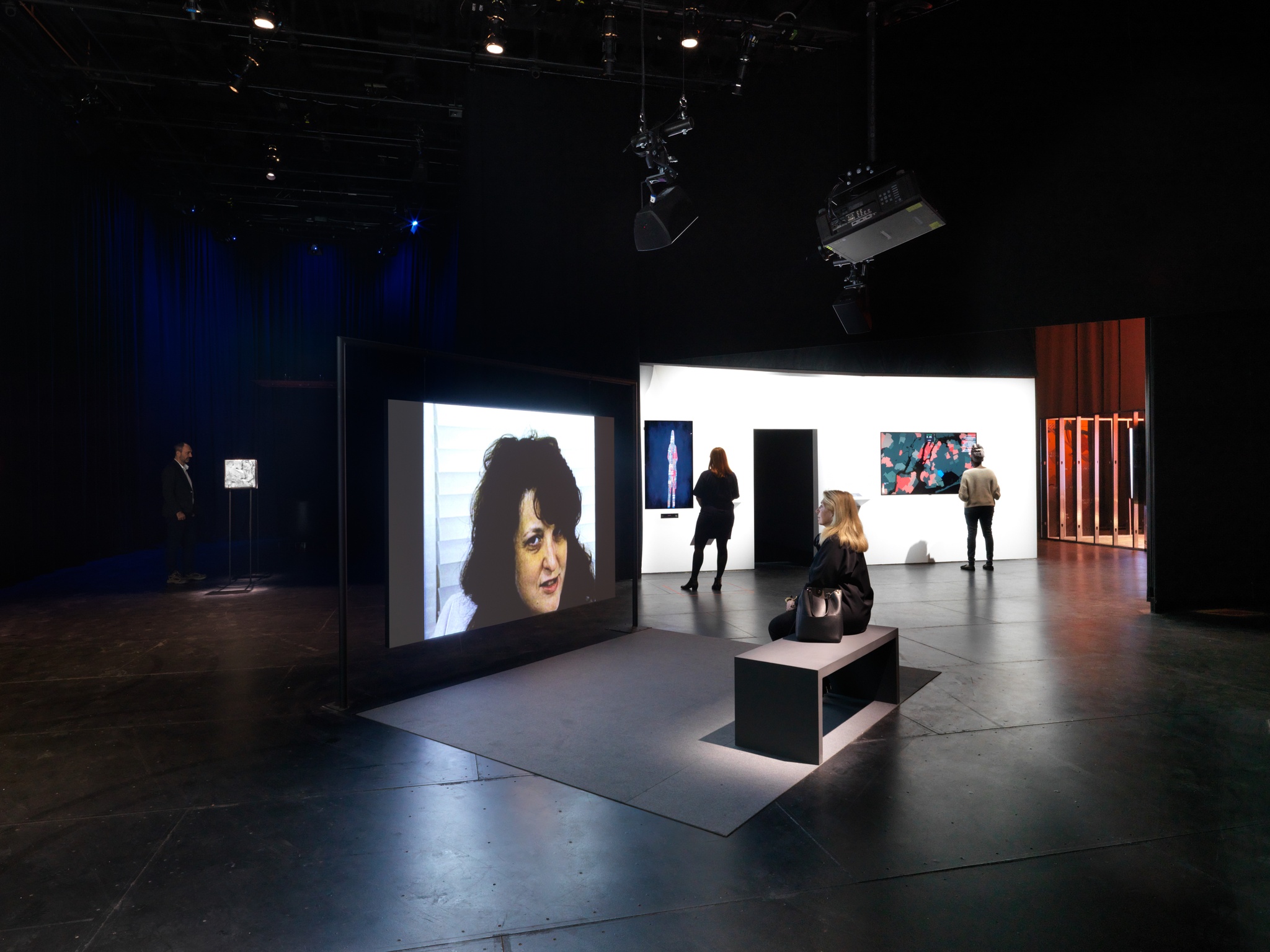 A view of the gallery for Manual Override with a woman watching a video by Lynn Hershman Leeson in the center of the room