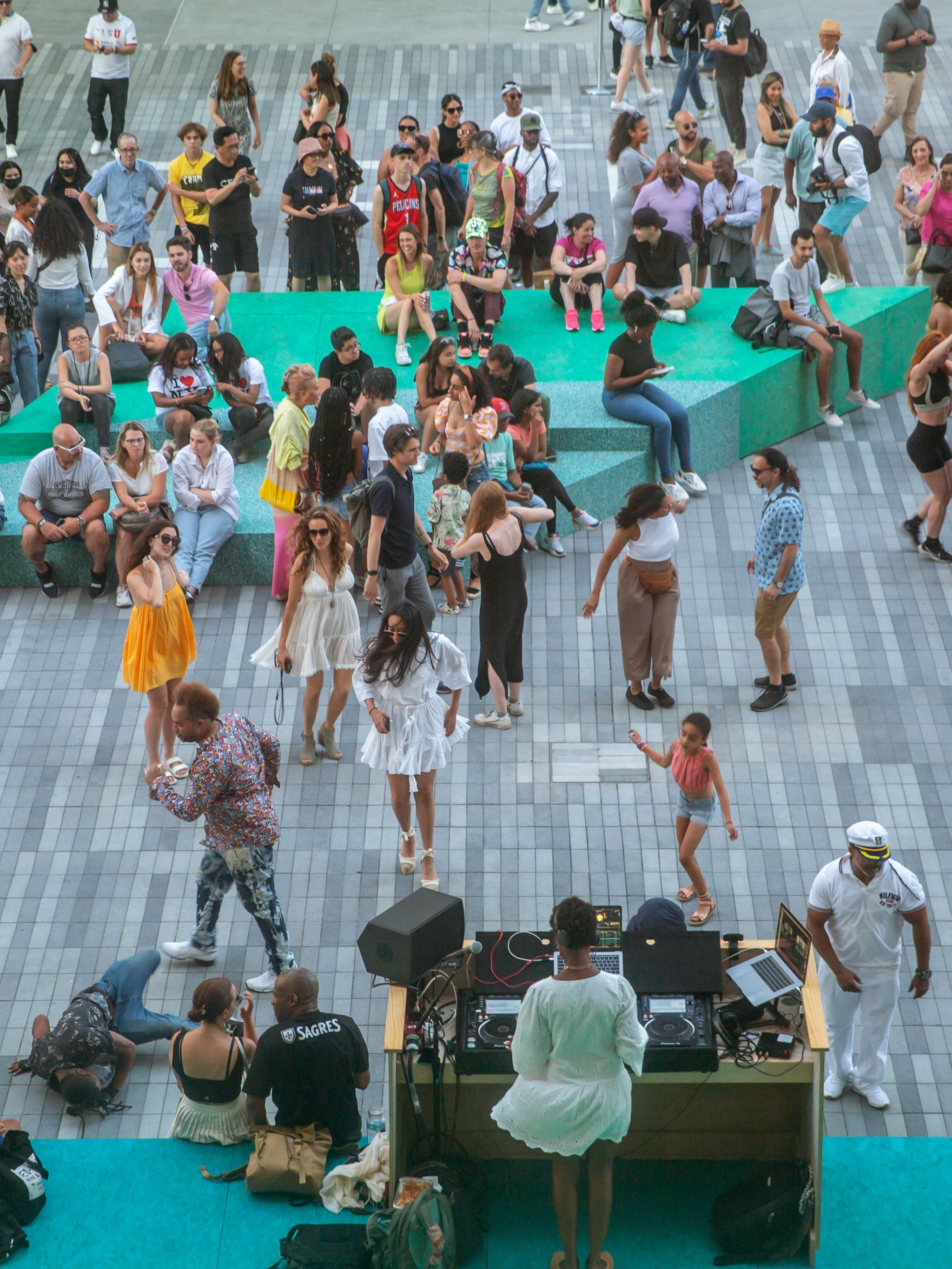 An aerial view of The Shed's outdoor Plaza where a crowd dances in the summer while a DJ in a short white dress being blown in the breeze spins.