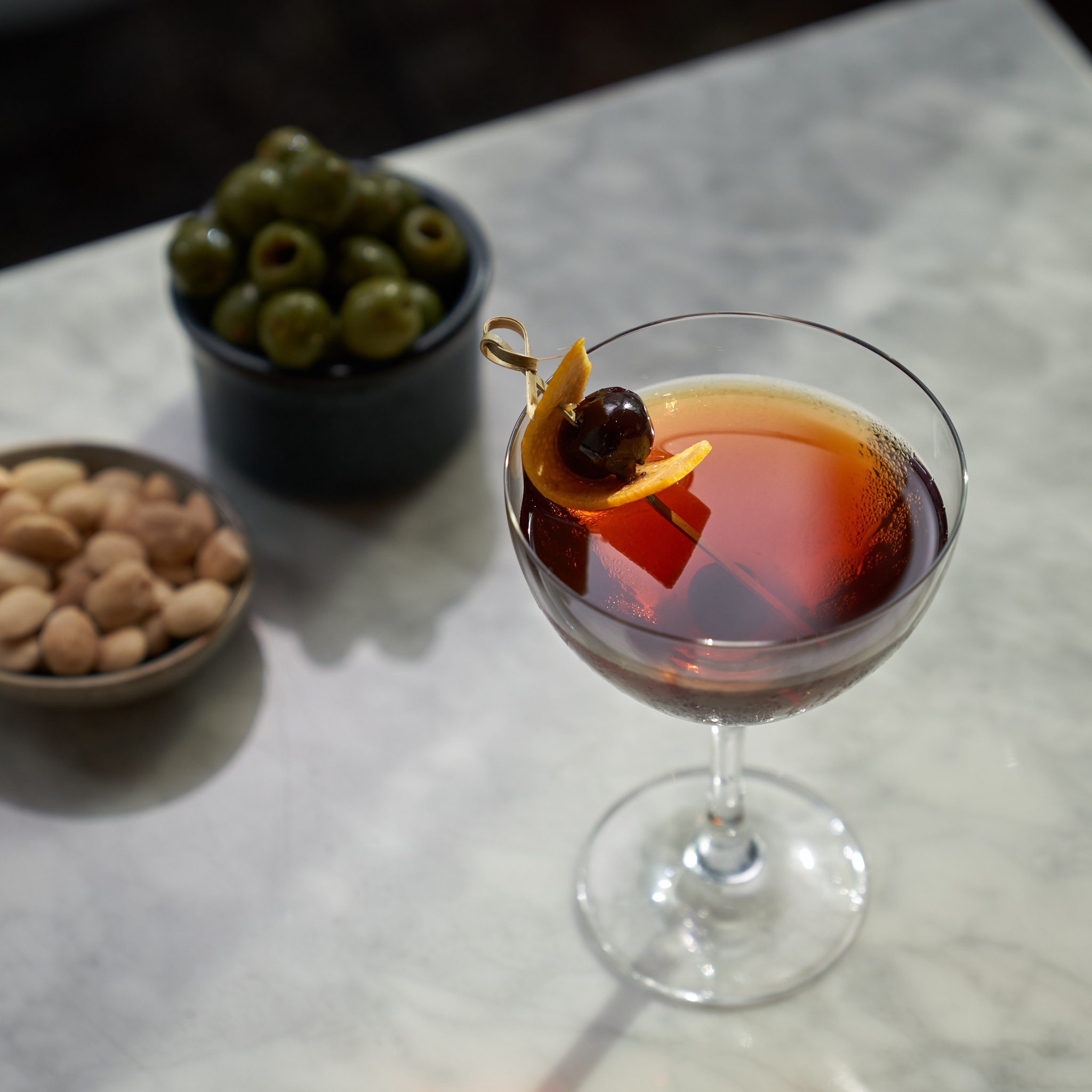 Image of a cocktail accompanied by olives and almonds.