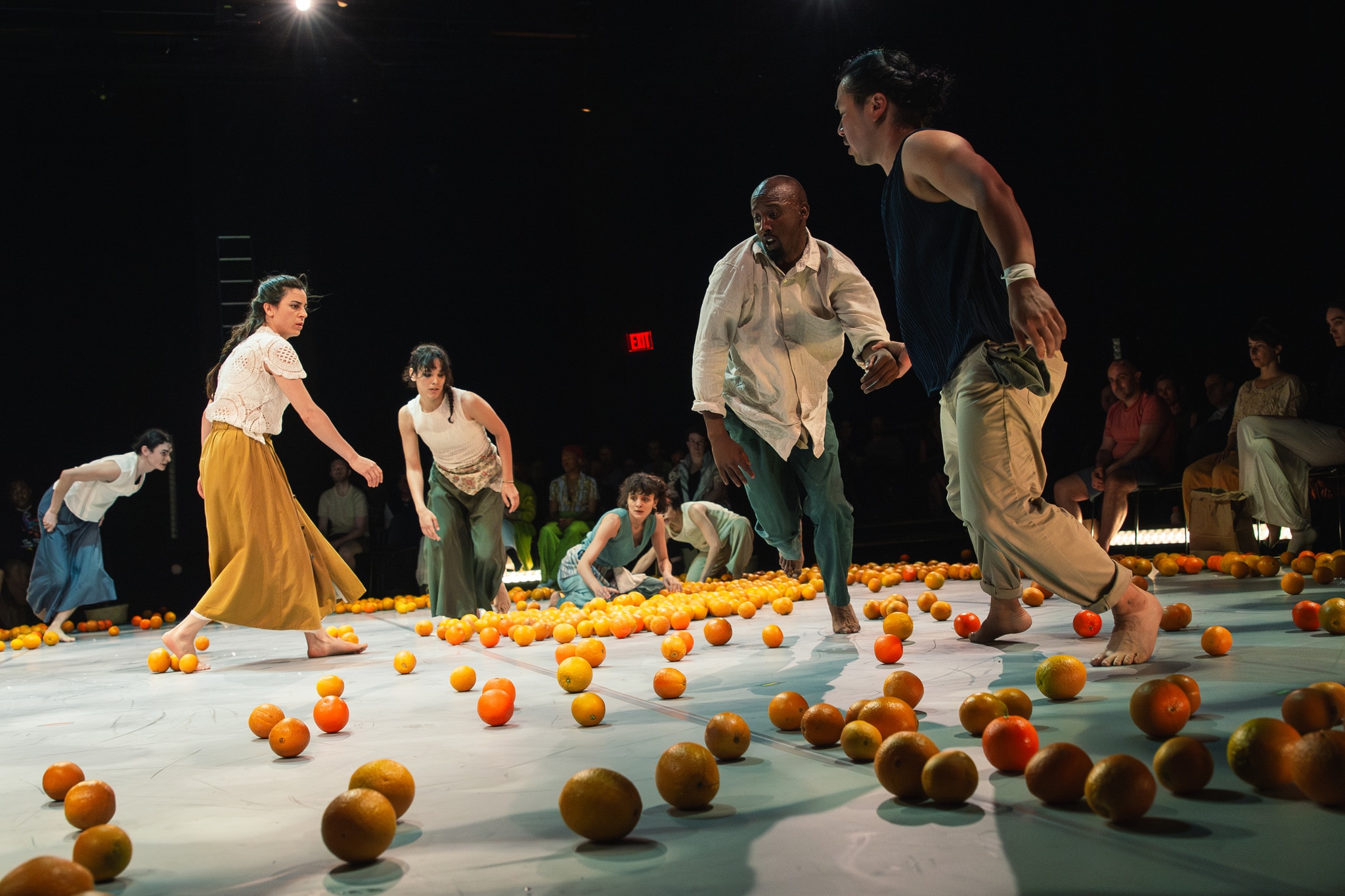 Dancers move energetically around a central performance space strewn with brightly colored oranges.