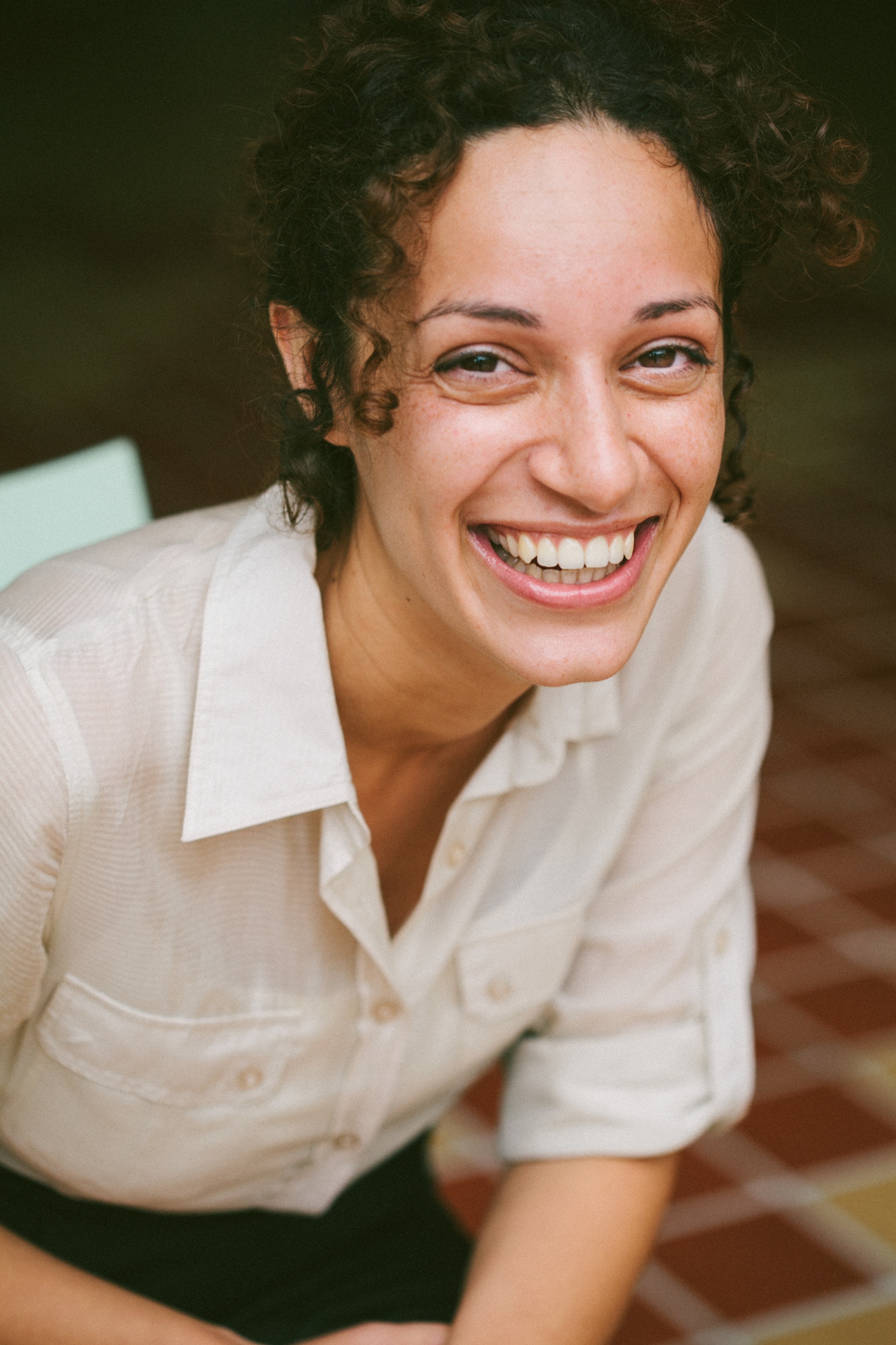 A photo of a smiling Maricelle Robles taken from slightly above. Robles wears a button down shirt with sleeves rolled up to her elbows.