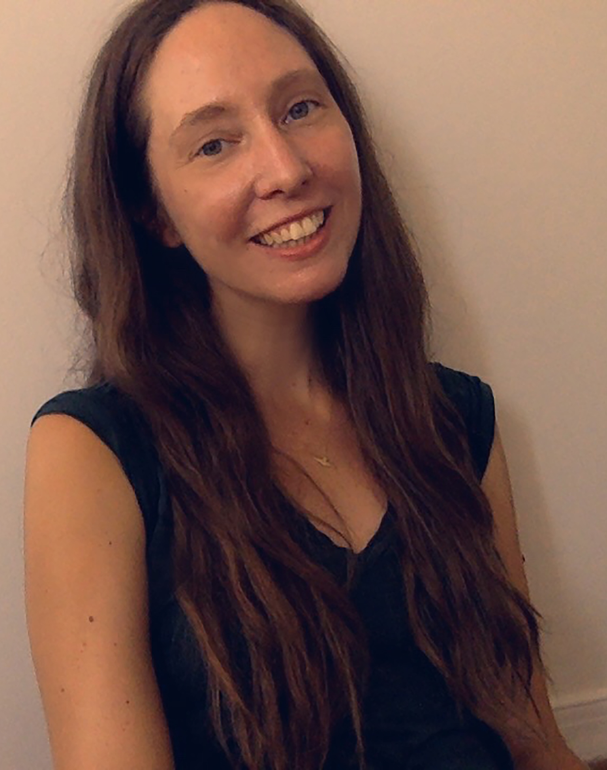 A photo of Kim Brandt in a v-neck shirt with hair falling over her shoulders. Brandt is smiling with her head slightly back. 