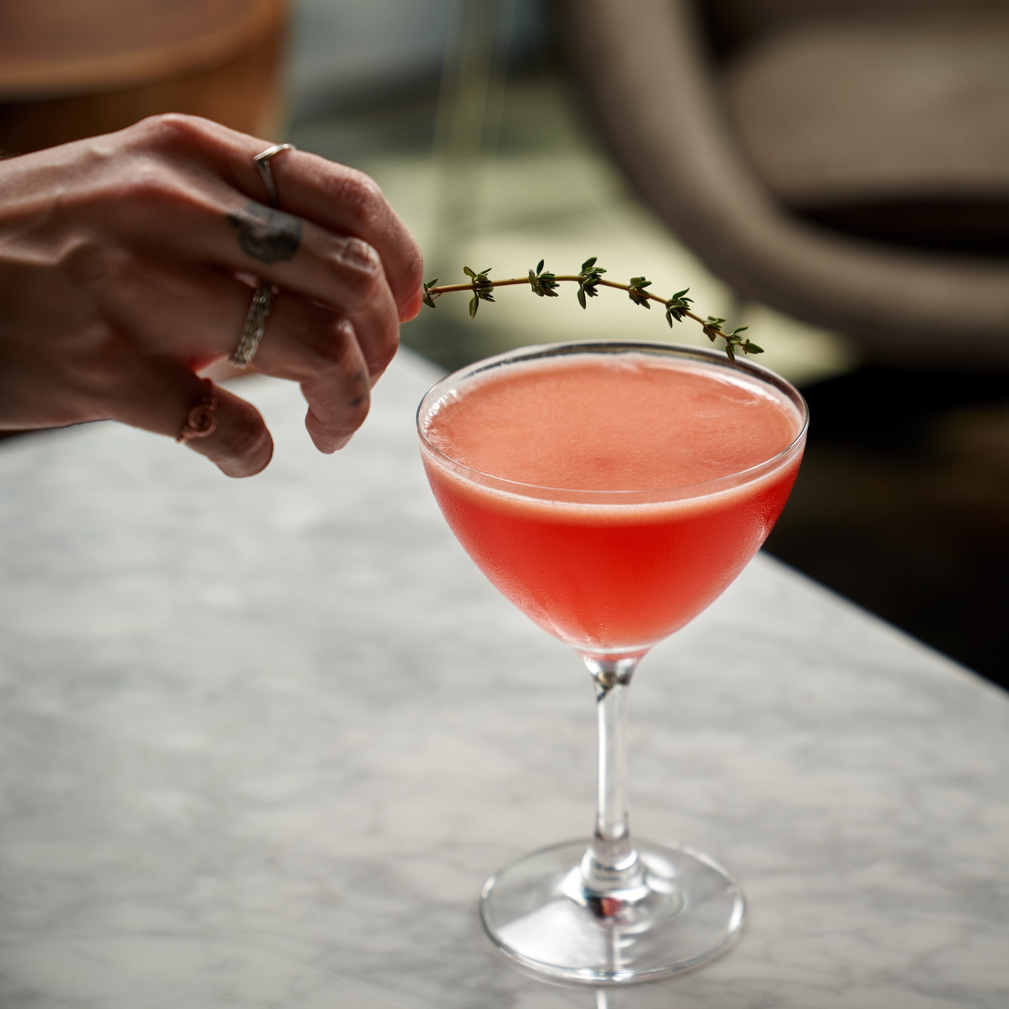 Image of a bartender decorating a cocktail with a sprig of thyme.