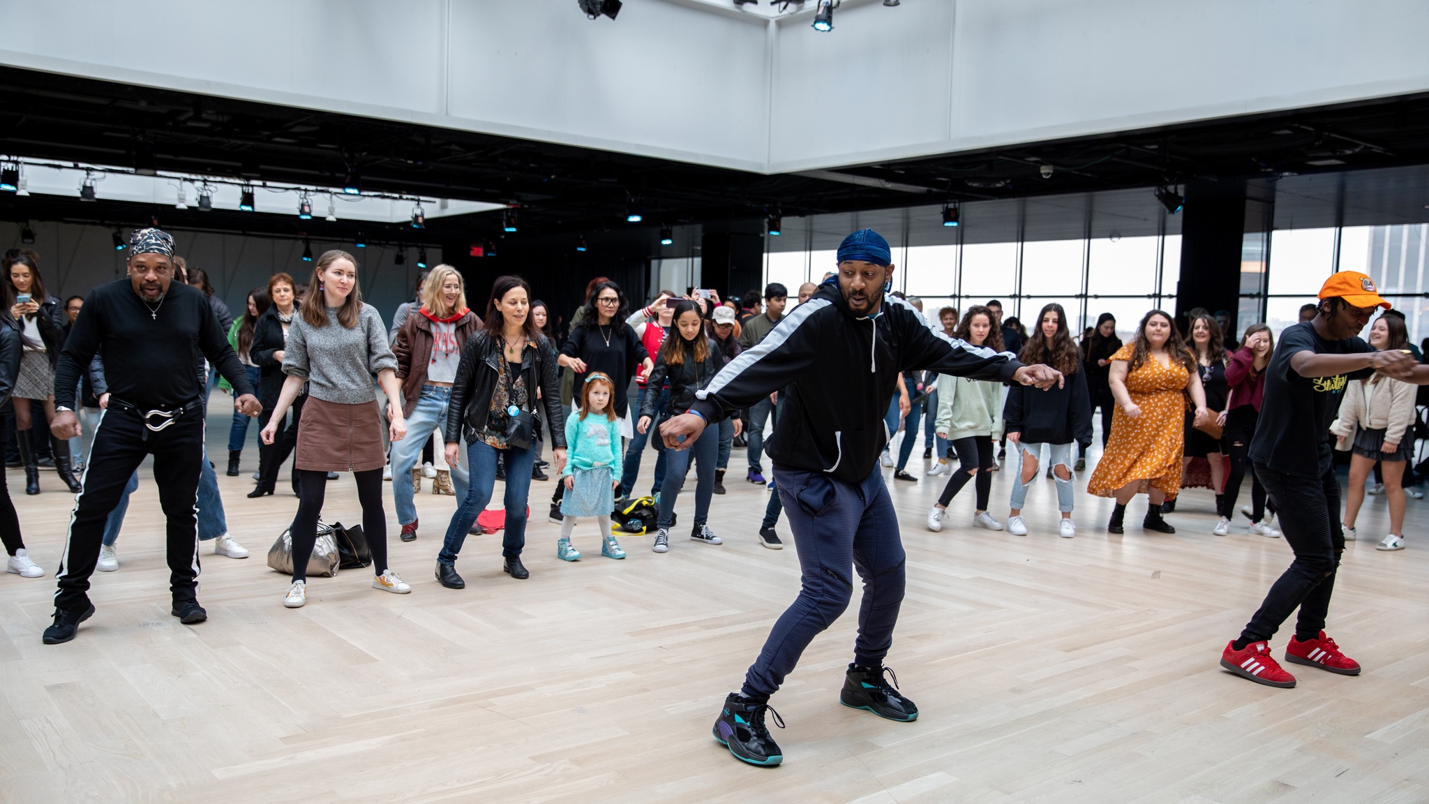 A man leading a dance workshop with participants behind him in a line in a well lit event space