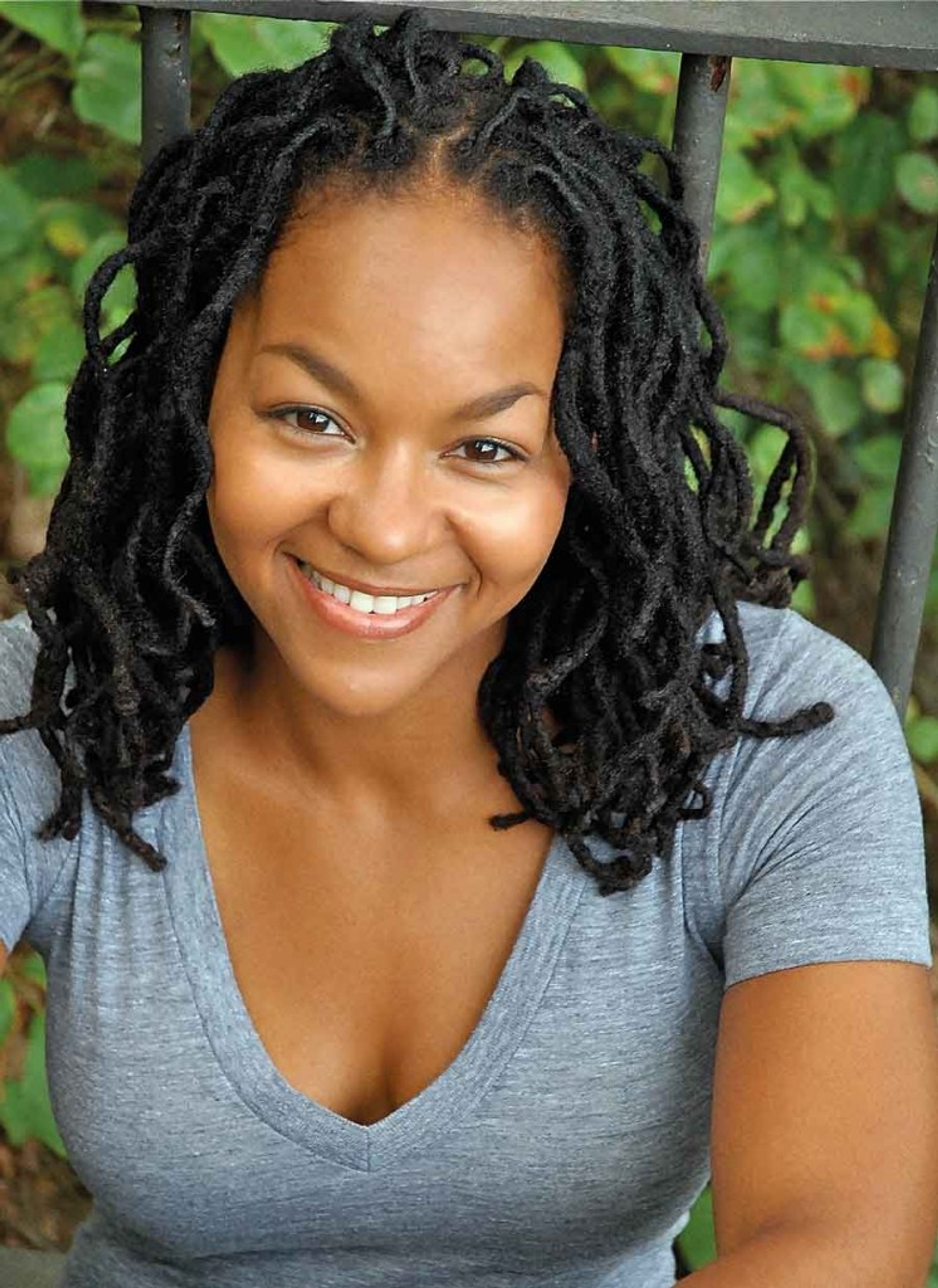 A portrait of Crystal Dickinson, smiling up at the camera and wearing a blue deep v-neck t-shirt