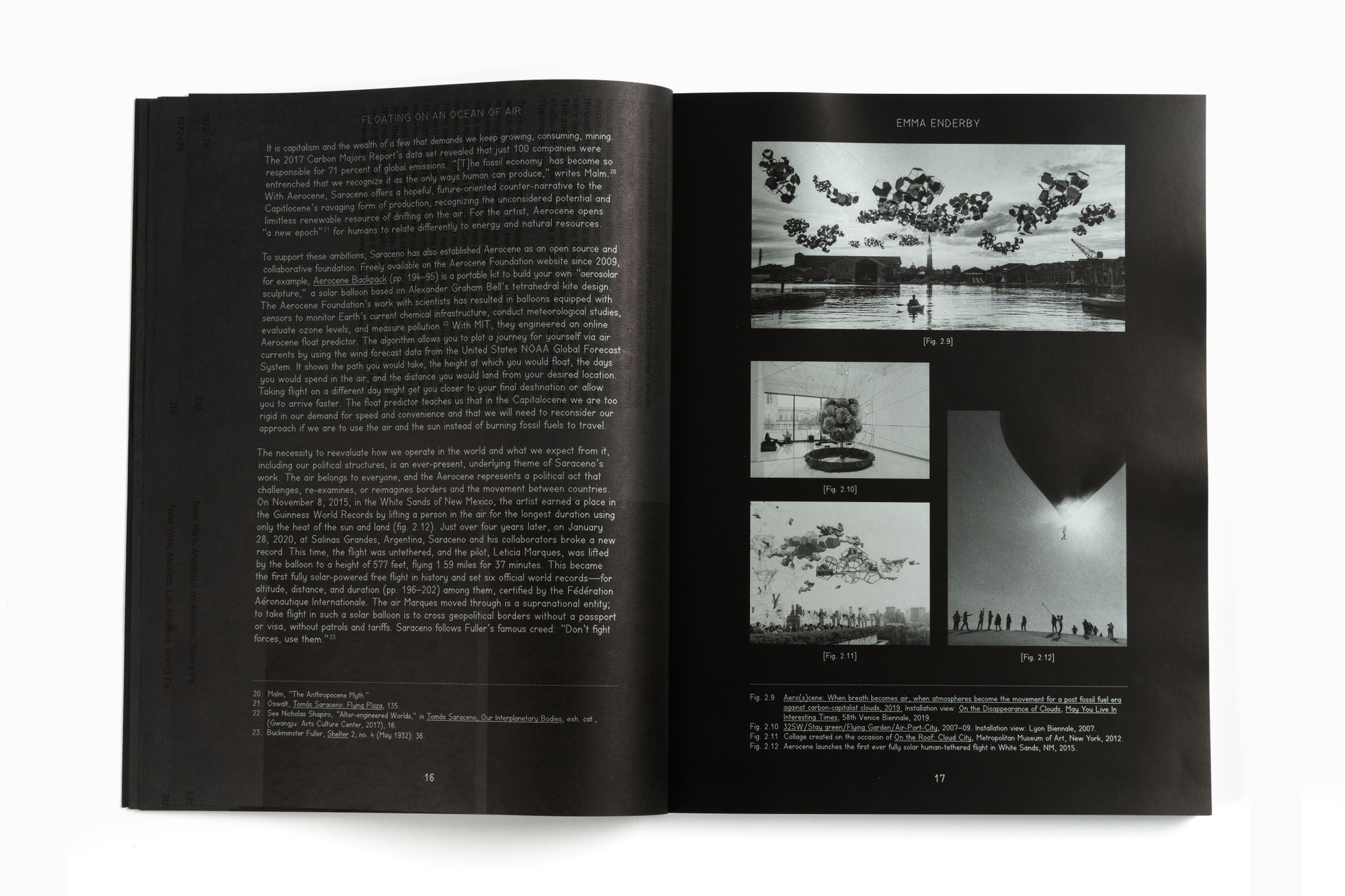 An exhibition catalogue lying open on a white surface. The book has black pages and text and images printed in silvery ink.