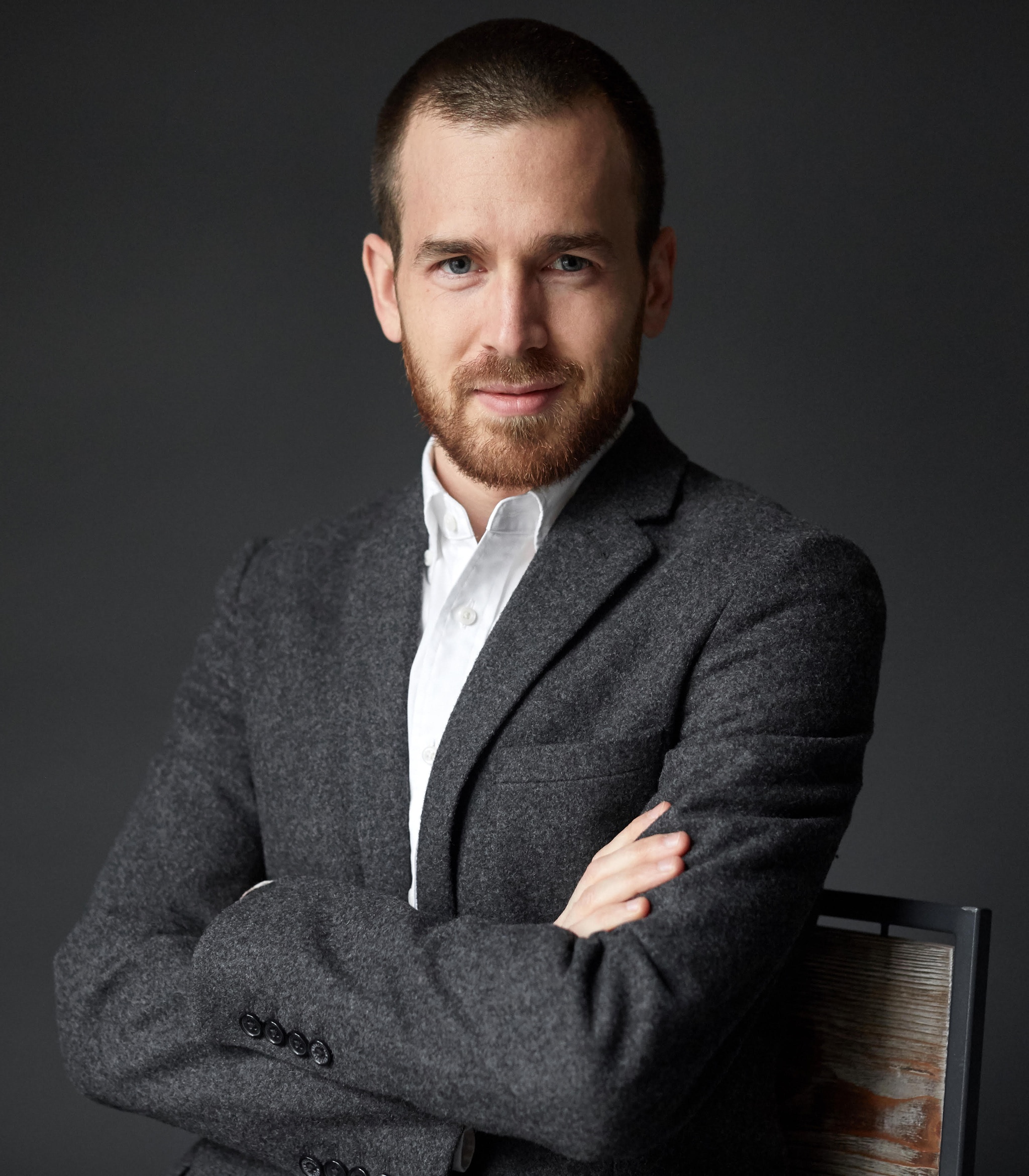 A photo of Daniel S. Palmer with arms crossed across his torso. Palmer wears a gray blazer and white shirt and looks into the camera. 