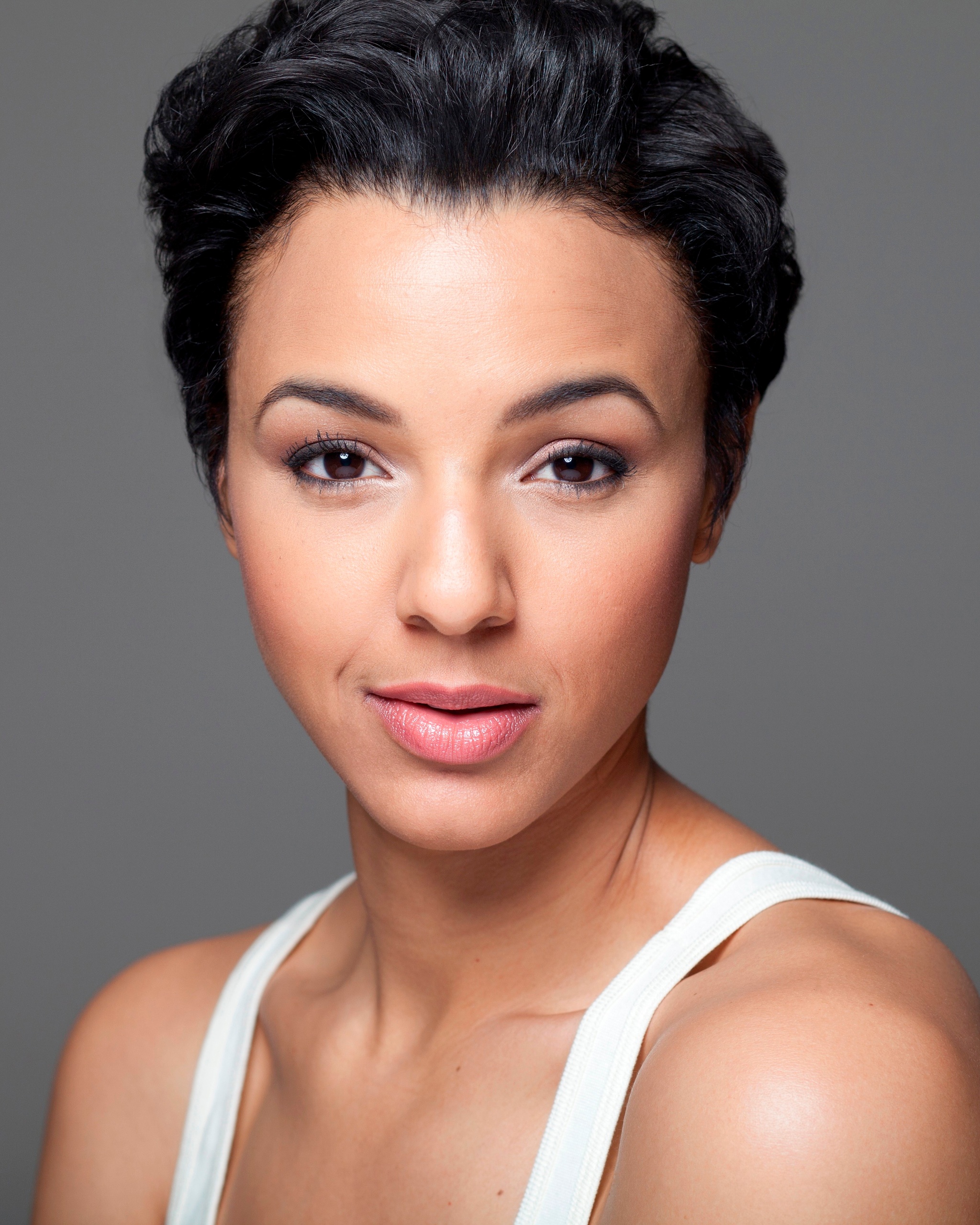 A portrait of Tiffany Rachelle Stewart, smiling with eyebrows arched and wearing a white tank top