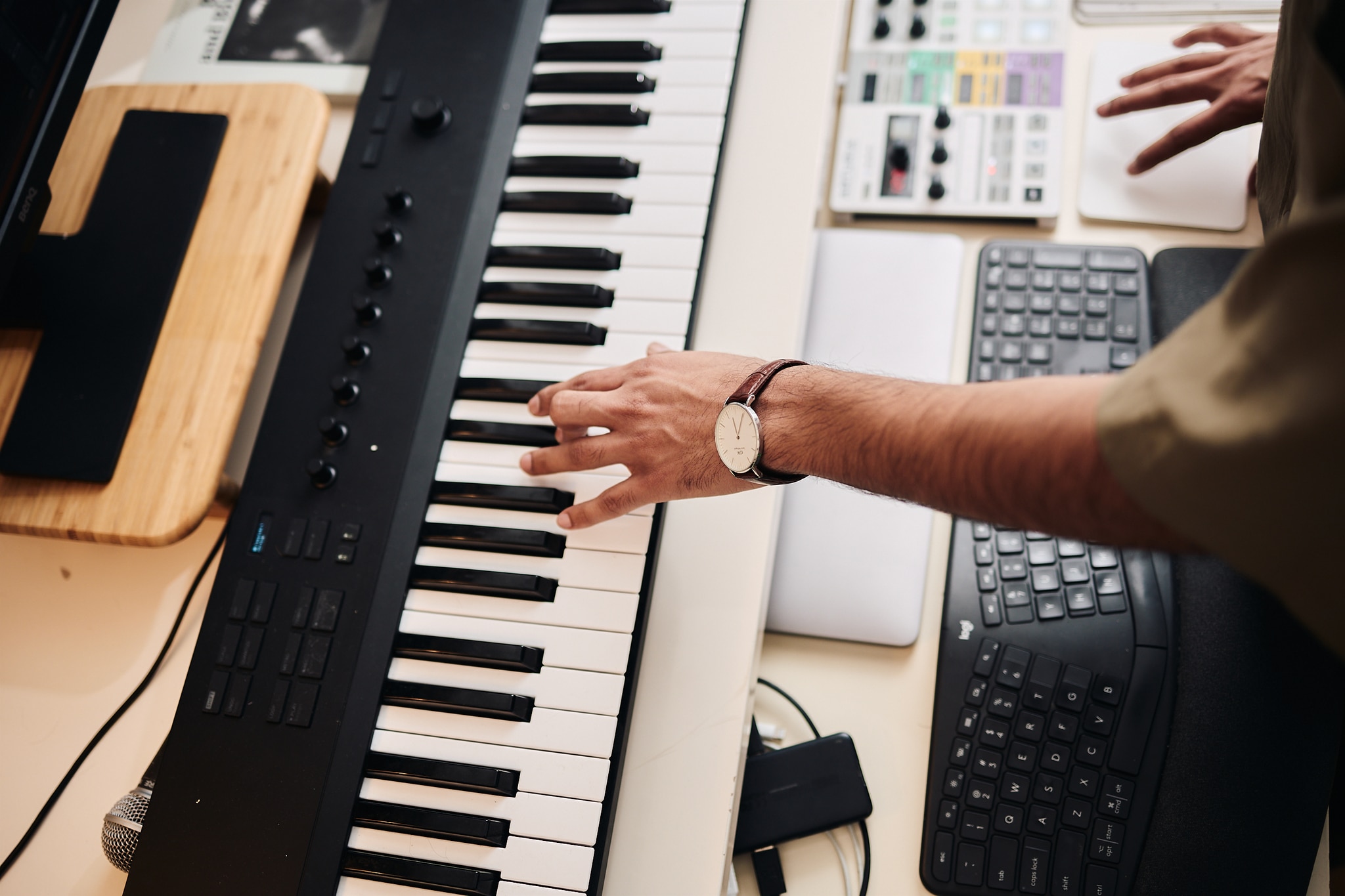 The hand and arm of artist Zain Alam are seen from above as he reaches out to play a piano keyboard.