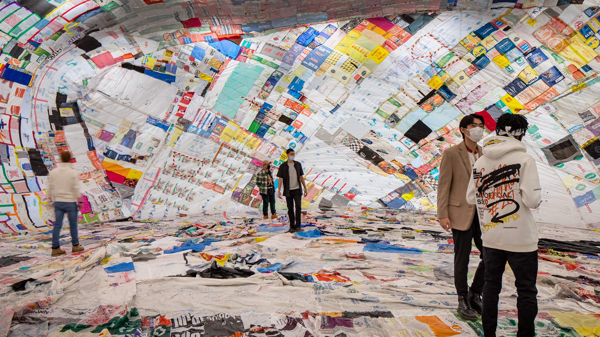 Five people stand inside a cavernous ballon made of a colorful patchwork of reused plastic bags quilted together with tape