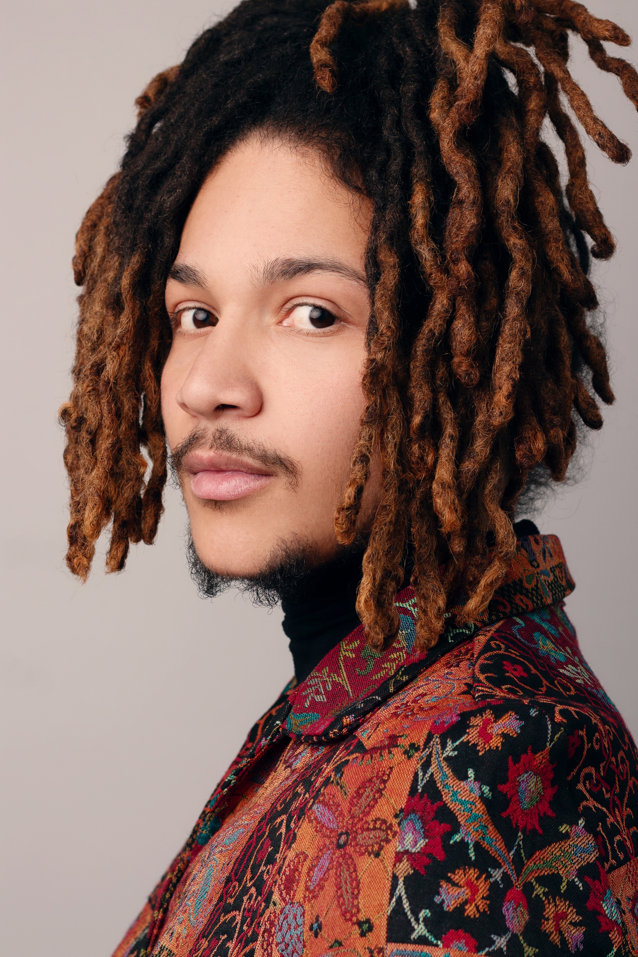 A portrait of Gabriel Ramirez, seen in profile with his face turned slightly so he looks at the camera. Ramirez wears a floral print jacket.