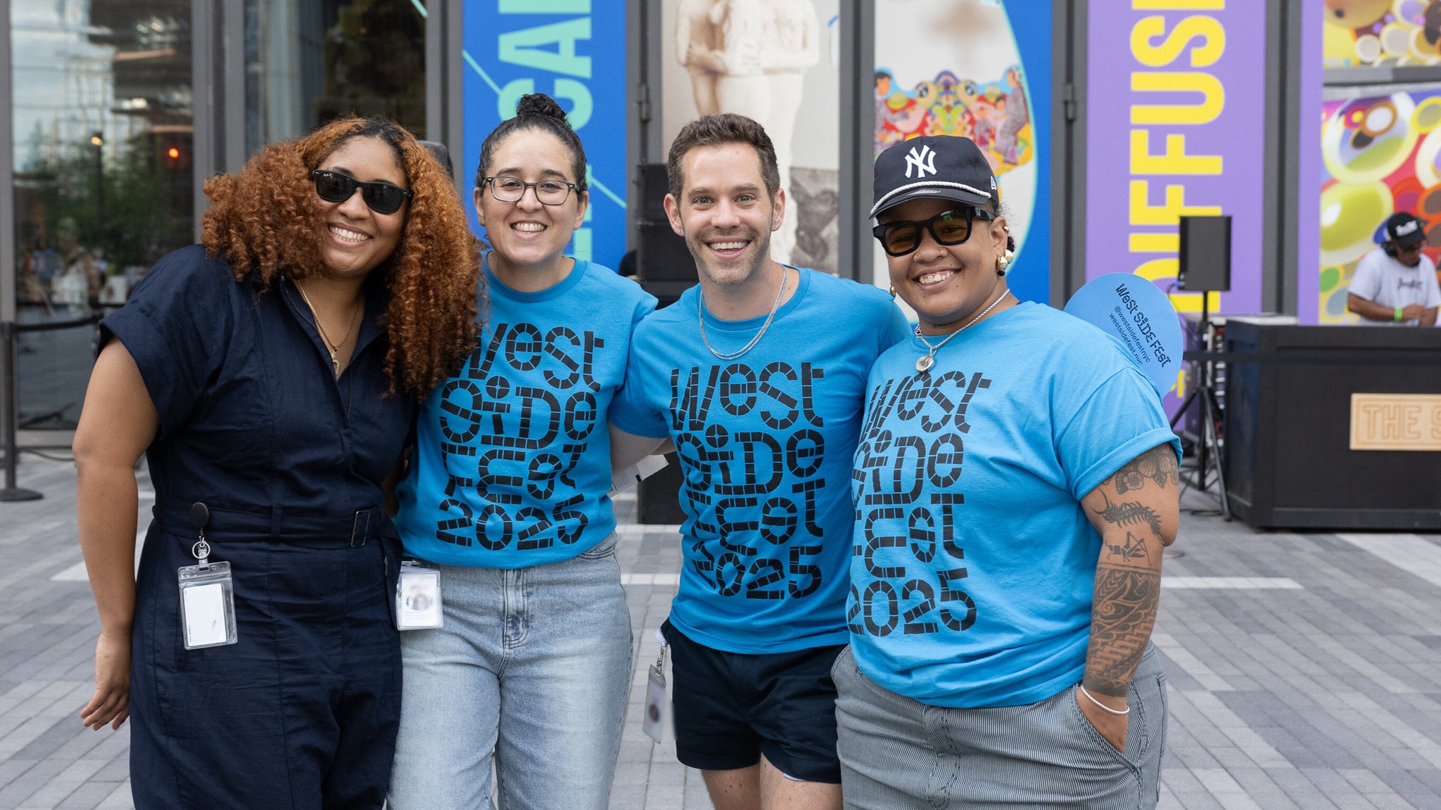 A group of four Shed staff members pose with arms over each others' shoulders. Three of the staff members were light blue t-shirts with West Side Fest branding.